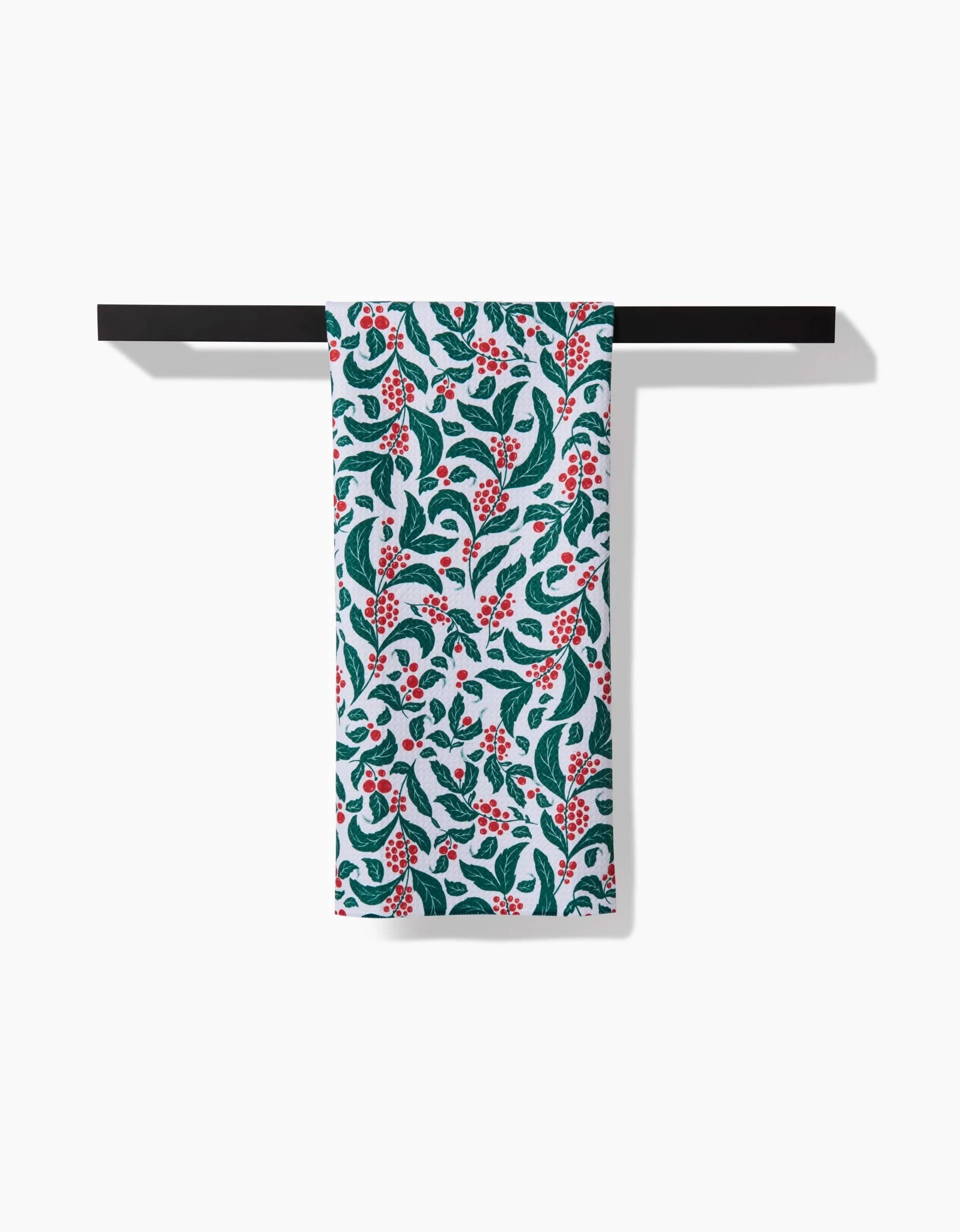 The Danelys Sidron Snowberry tea towel, featuring green leaves and red berries on white ultra-absorbent recycled fabric, hangs neatly on a black towel bar against a plain white background.