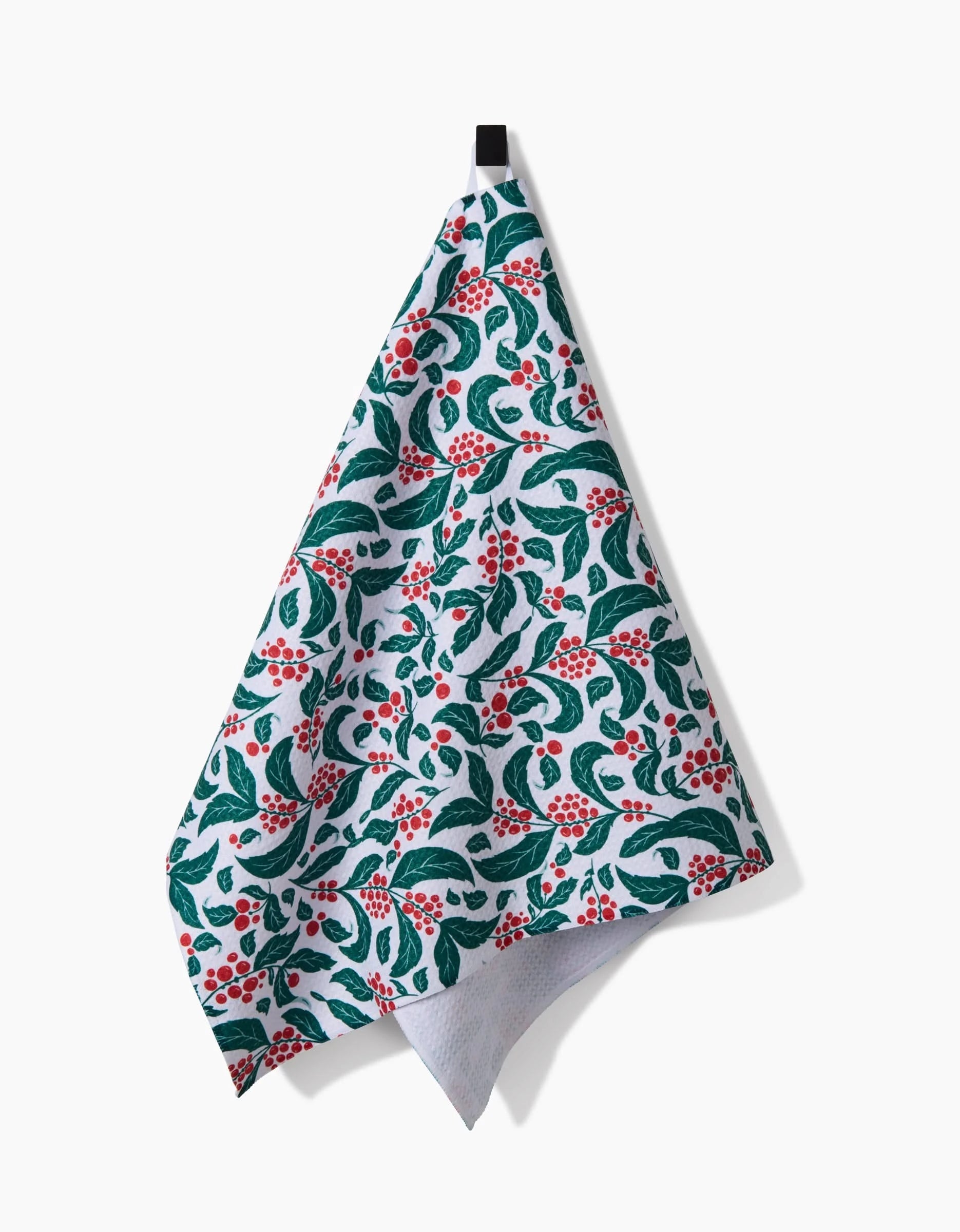 The Danelys Sidron Snowberry tea towel, made from recycled materials, features a green leaf and red berry pattern on white fabric and hangs from a black loop against a plain white background.