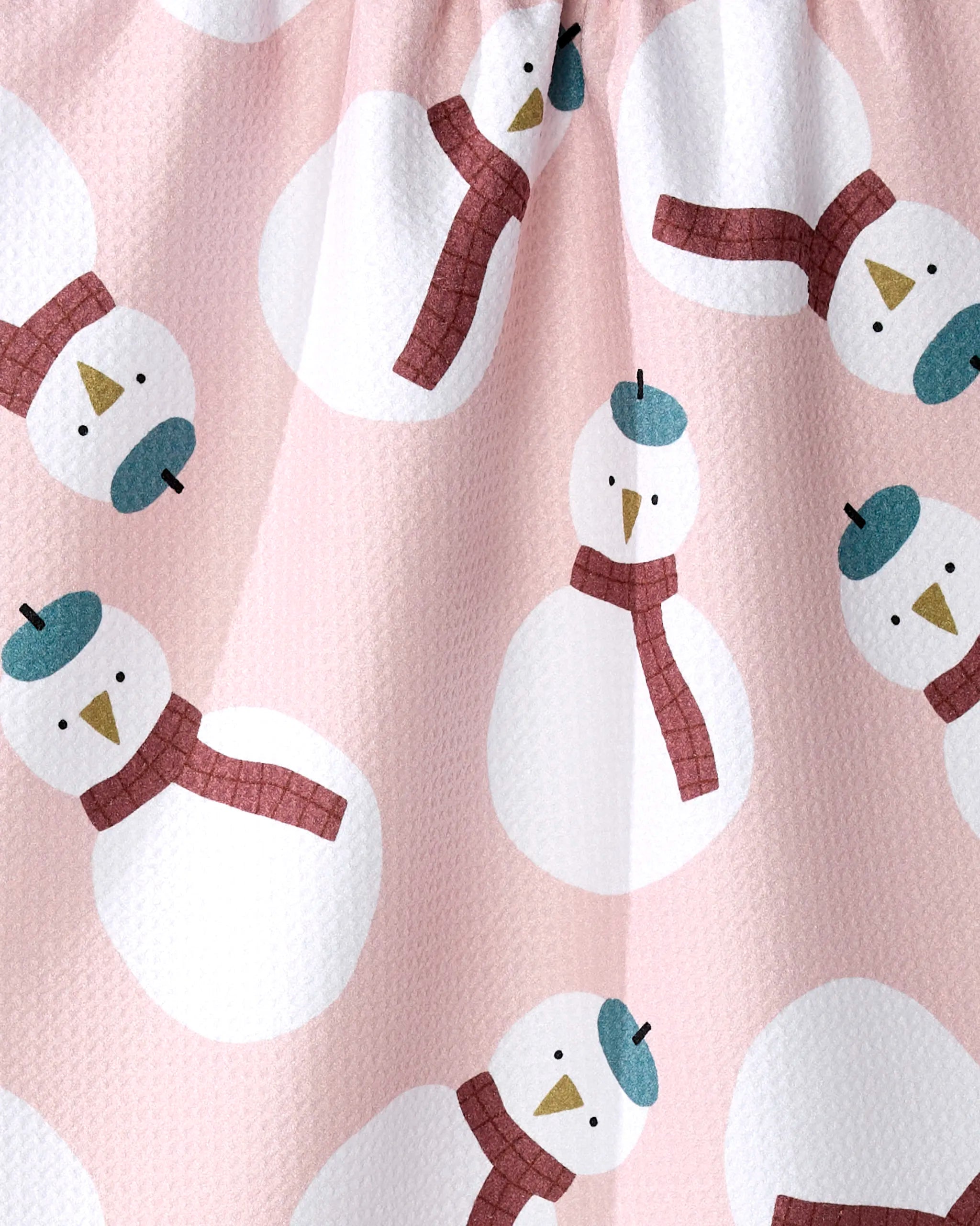 The Snowman tea towel by Jennifer Bouron is pink, textured, and made from recycled materials. It features a repeating pattern of white snowmen with red scarves, blue hats, and carrot noses in various directions.