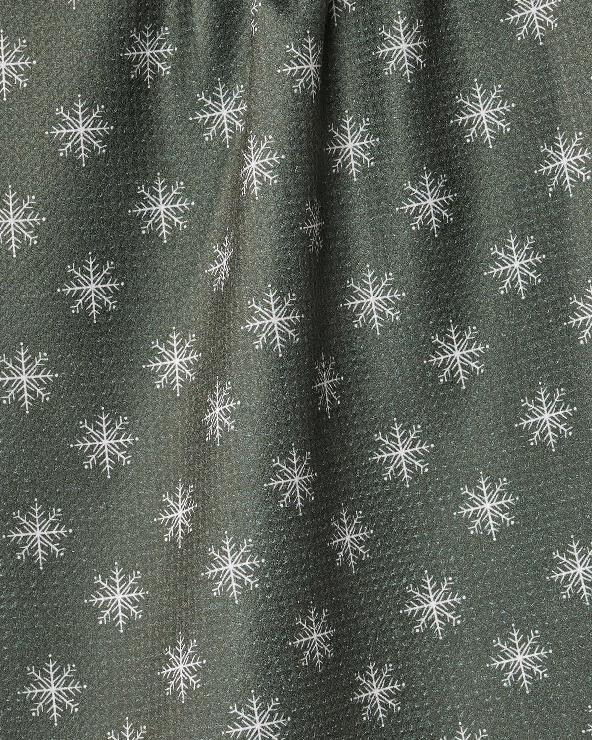 Snowy by Geometry features a dark green fabric with a subtle texture, adorned with a repeating pattern of white snowflakes. Slight gathering at the top creates gentle vertical folds, while the ultra-absorbent tea towel is made from recycled materials—blending sustainability, function, and charm.