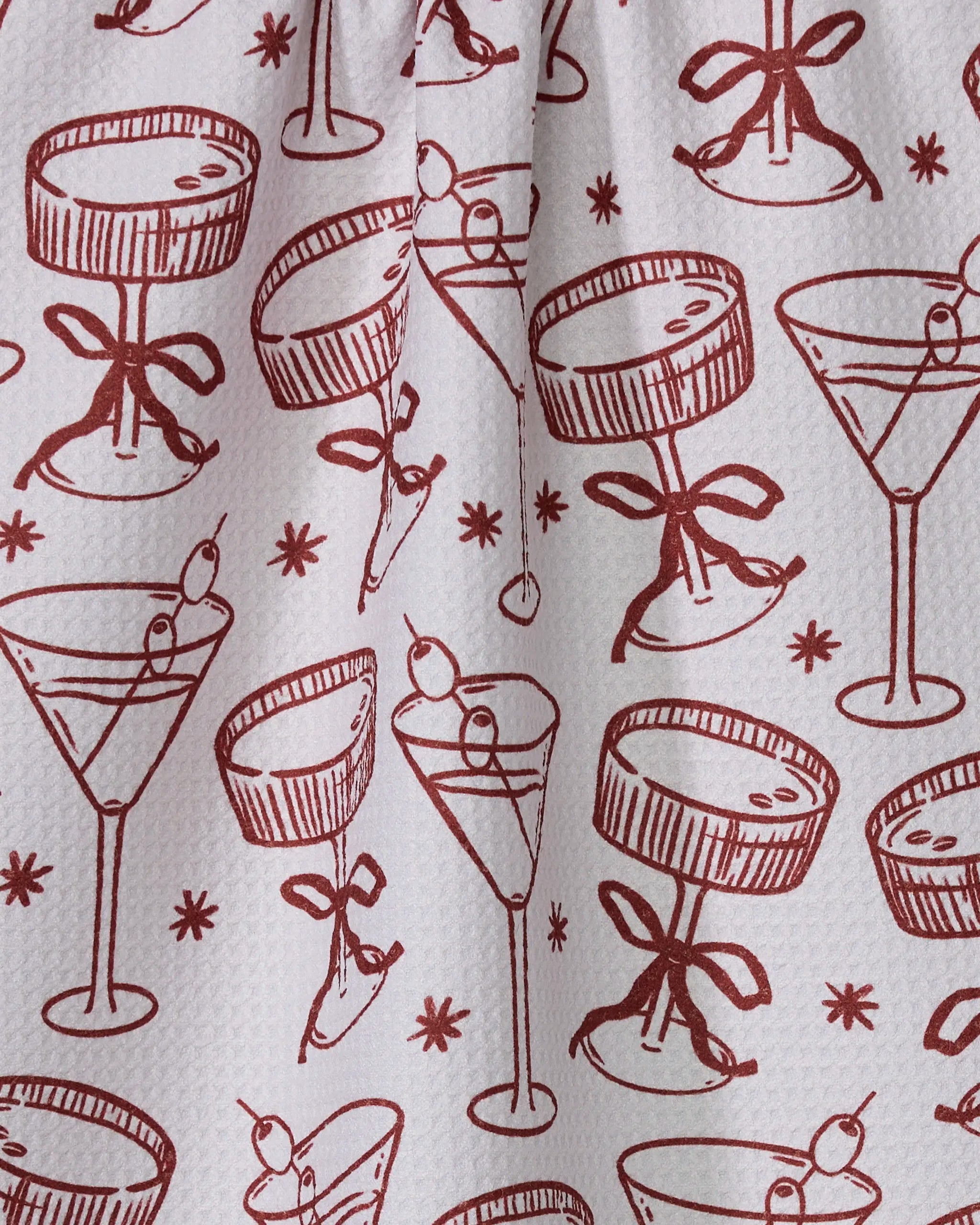 The Geometry Soiree tea towel features red line drawings of cocktail glasses with olives and bows plus star accents on white, all made from quick-drying recycled materials for eco-friendly style.