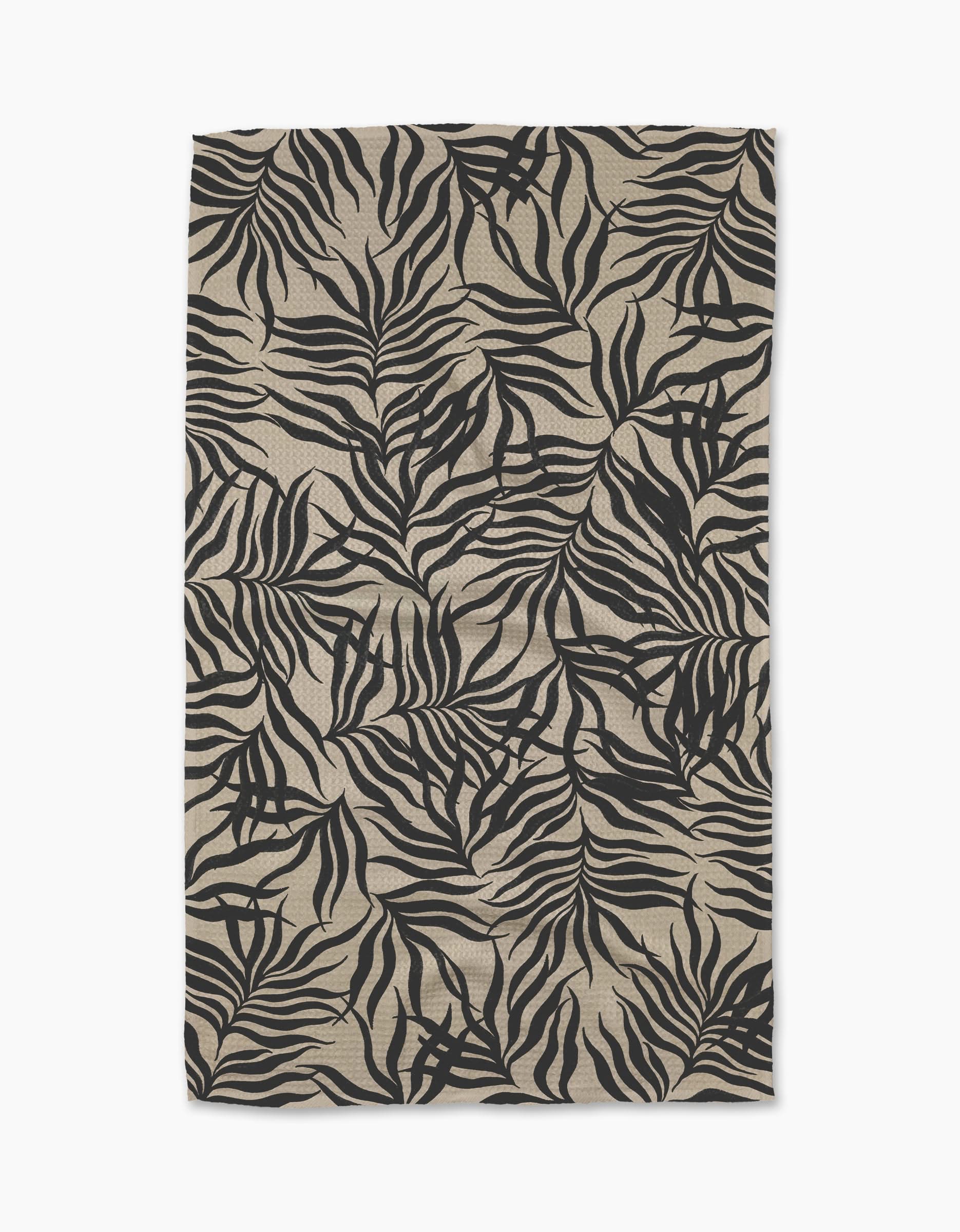 A rectangular beige Geometry Solar Flare tea towel from Geometry, featuring a bold black tropical leaf pattern on Geoweave fabric with slight wrinkles, photographed against a white background.
