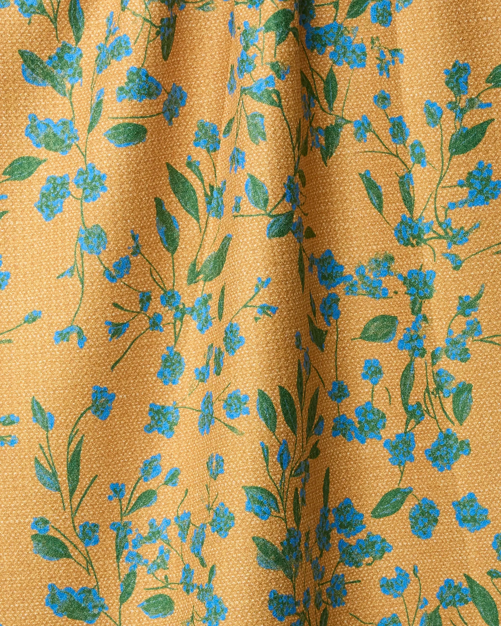 The Soleado towel by Geometry is made from yellow fabric with a subtle dotted texture, featuring a green leaf and blue flower pattern. The ultra-absorbent material has gentle folds, creating light shadows and highlights on its surface.