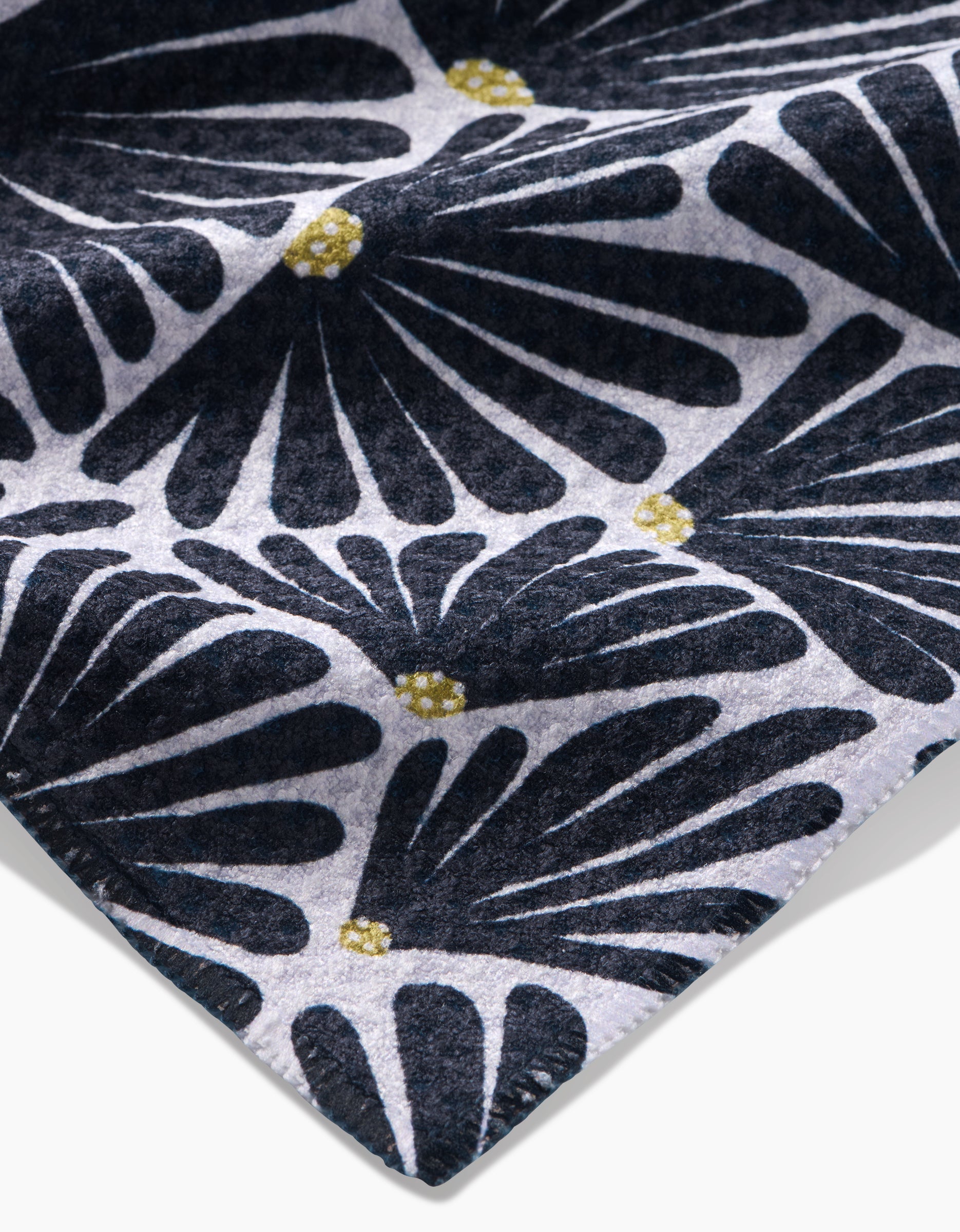A close-up of an Amy MacCready Solie Black Tea Towel shows ultra-absorbent Geoweave™ fabric with a repeating navy blue floral pattern and small yellow centers on a light grey background, neatly stitched along the edge.