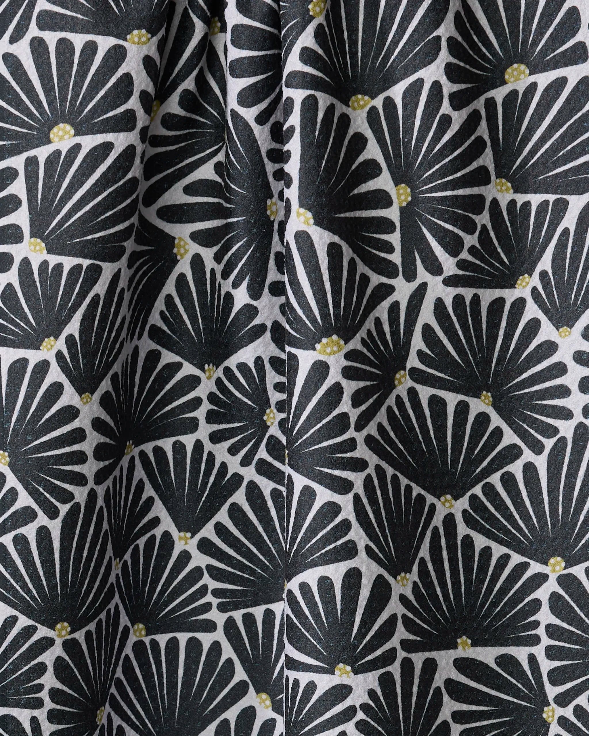 The Solie Black kitchen towel by Amy MacCready features a black fan-shaped leaf pattern with small yellow dots on light gray recycled fabric. Quick-drying with gentle folds and shadows, it adds depth and texture to your kitchen.