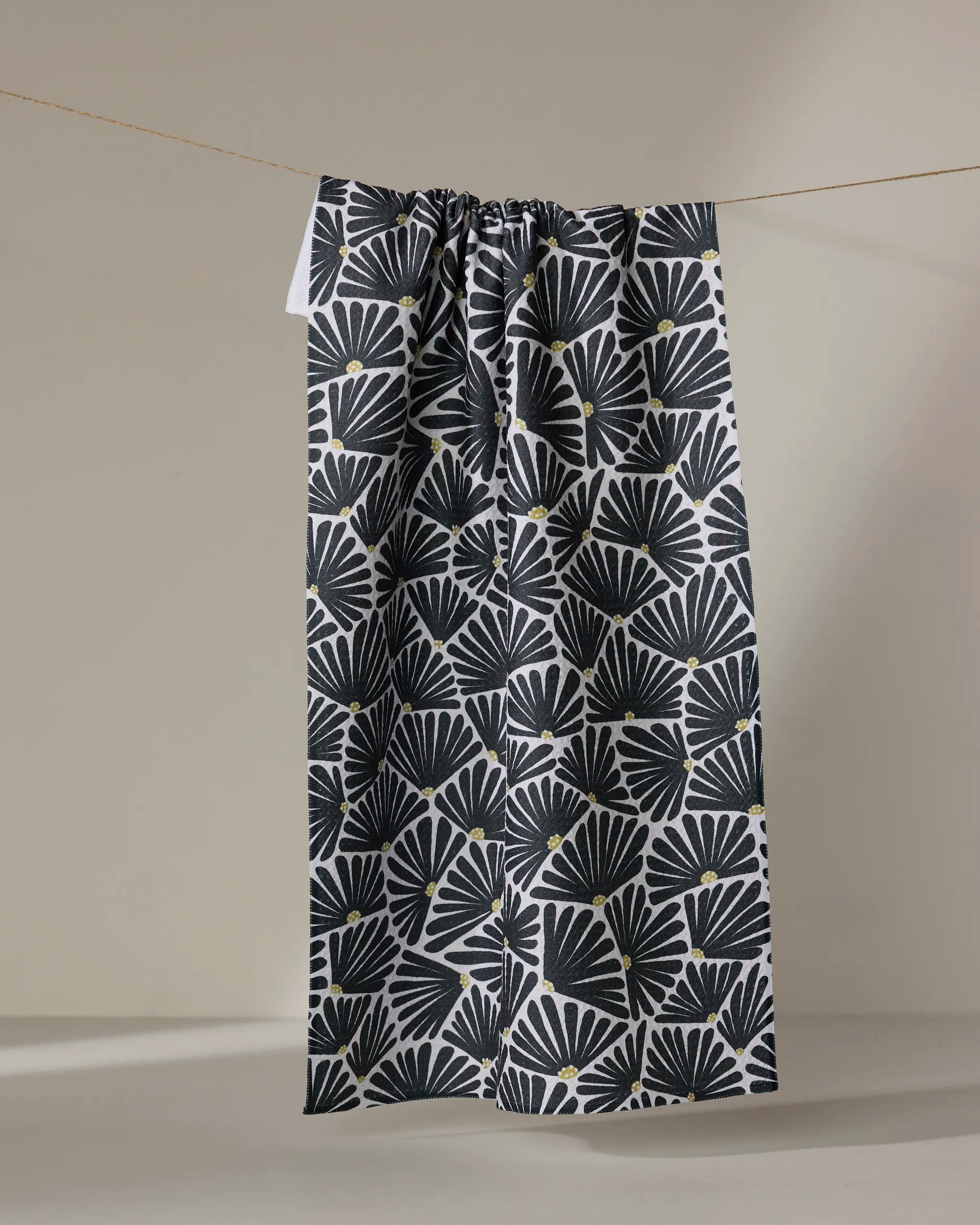 The Solie Black kitchen towel by Amy MacCready, featuring a recycled black and white fan pattern with small yellow dots, hangs on a string against a plain light background.