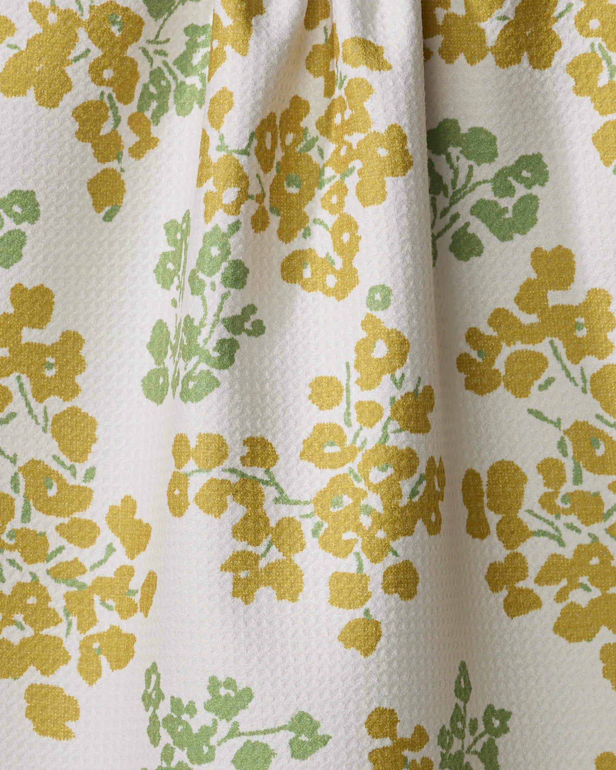 A close-up of the Geometry Sonnet Butter quick-drying towel, featuring white textured fabric adorned with yellow and green floral patterns of small clustered flowers and leaves.