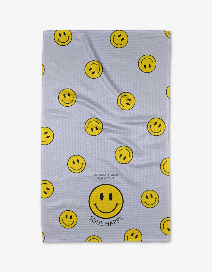 The “Soul Happy” tea towel by Quotes by Christie features multiple yellow smiley faces and a large one at the bottom, made from soft Geoweave™ fabric. SOUL HAPPY is printed below the large face, with DO MORE OF WHAT MAKES YOUR above it.