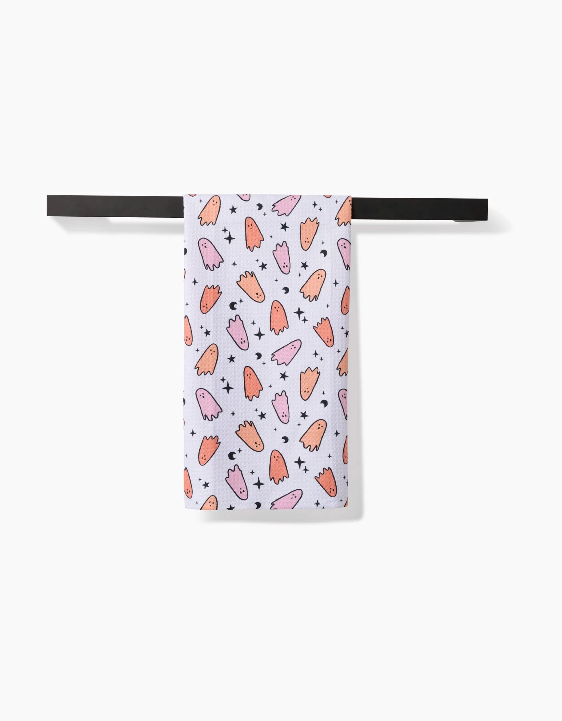 The Hufton Studio Space Ghosts Pink Orange tea towel, made from recycled materials, features orange and pink cartoon ghosts with black stars and hangs neatly on a black towel bar against a white background.