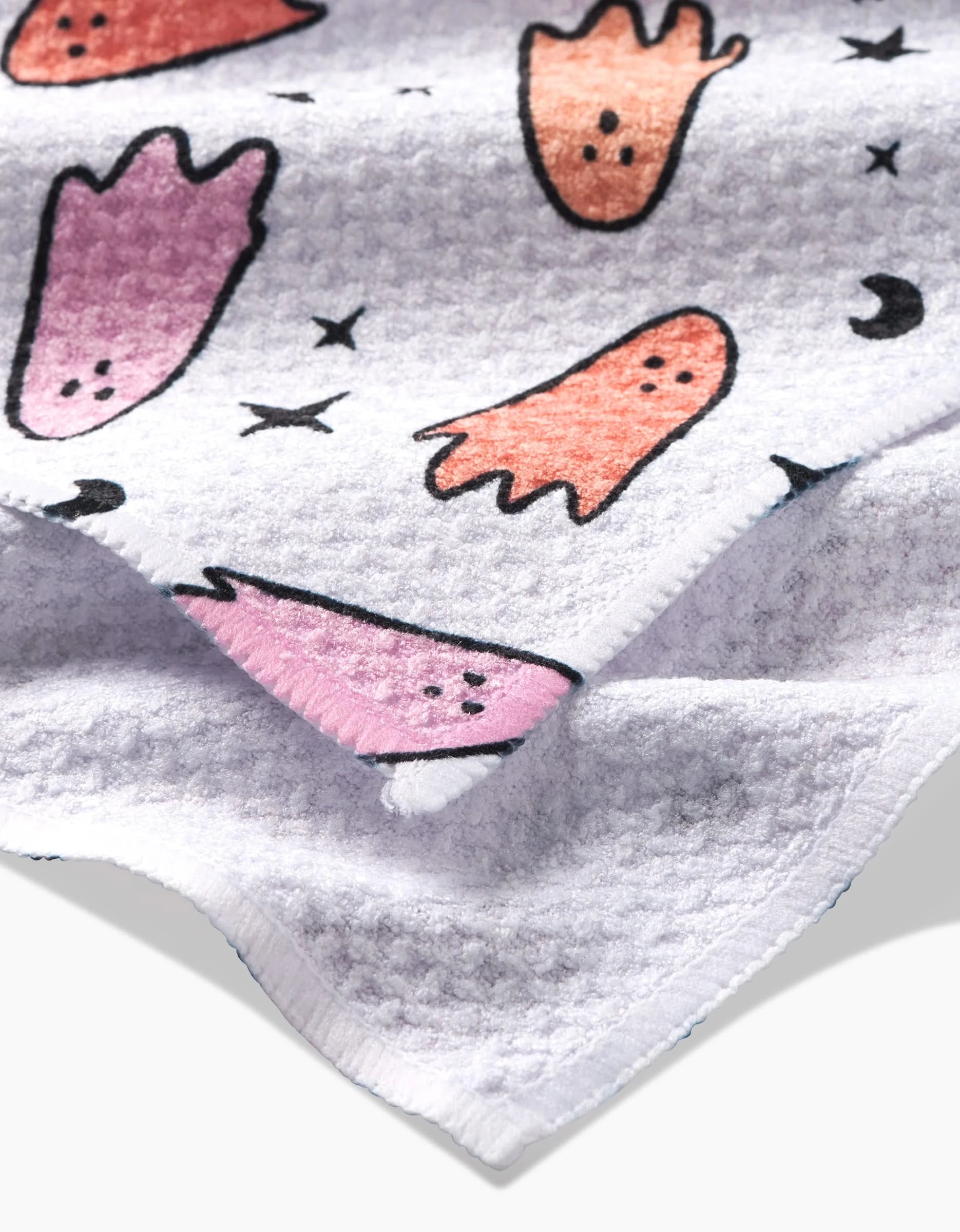 A close-up of Hufton Studio’s Space Ghosts Pink Orange tea towel, quick-drying and decorated with pink and orange ghosts, black stars, and crescent moons on a soft white background.