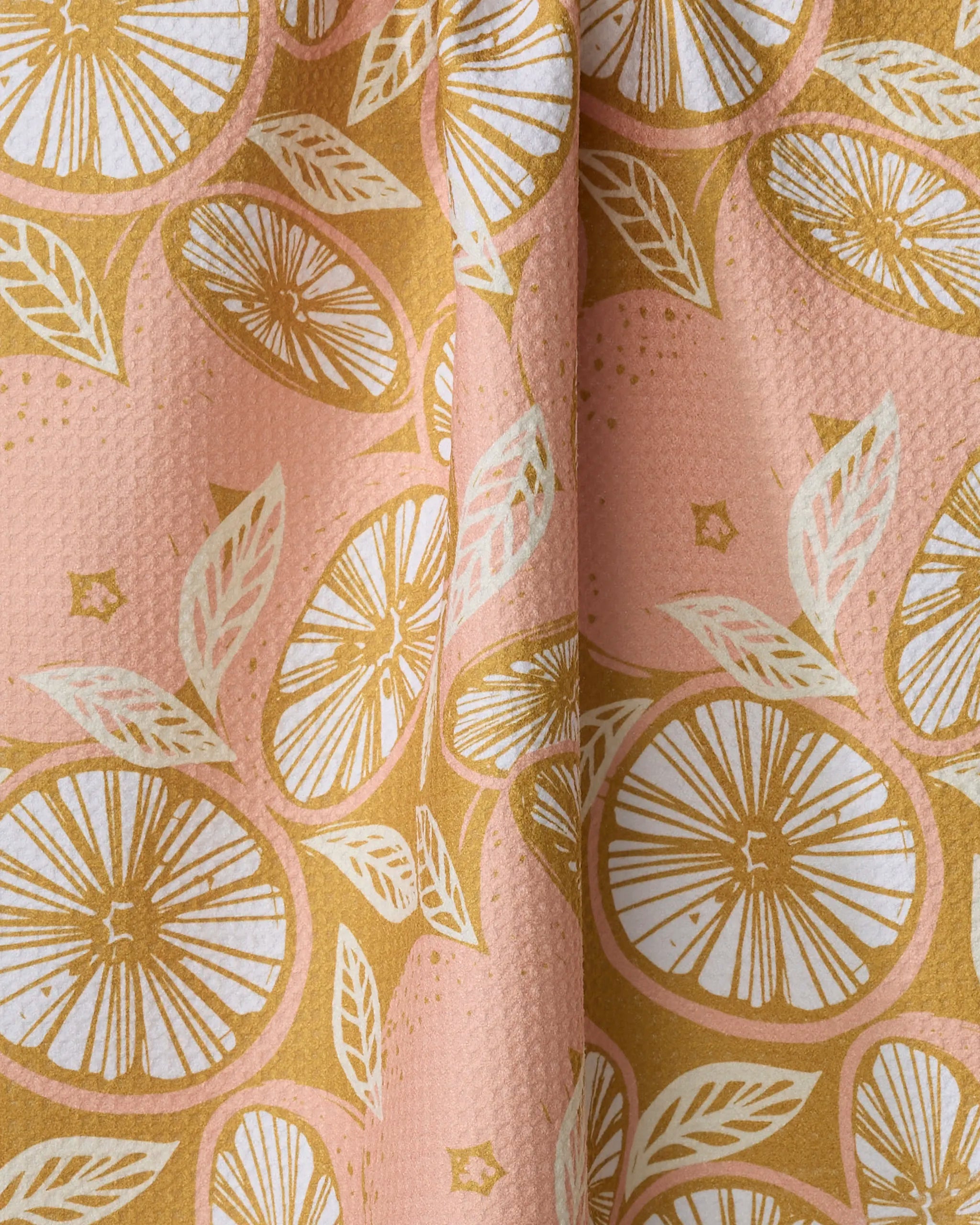 Close-up of Elisabeth Wing's Spanish Grapefruit towel: pink background with stylized orange citrus slices and white leaves. Quick-drying, slightly textured fabric draped in soft folds for a fresh, vibrant look.