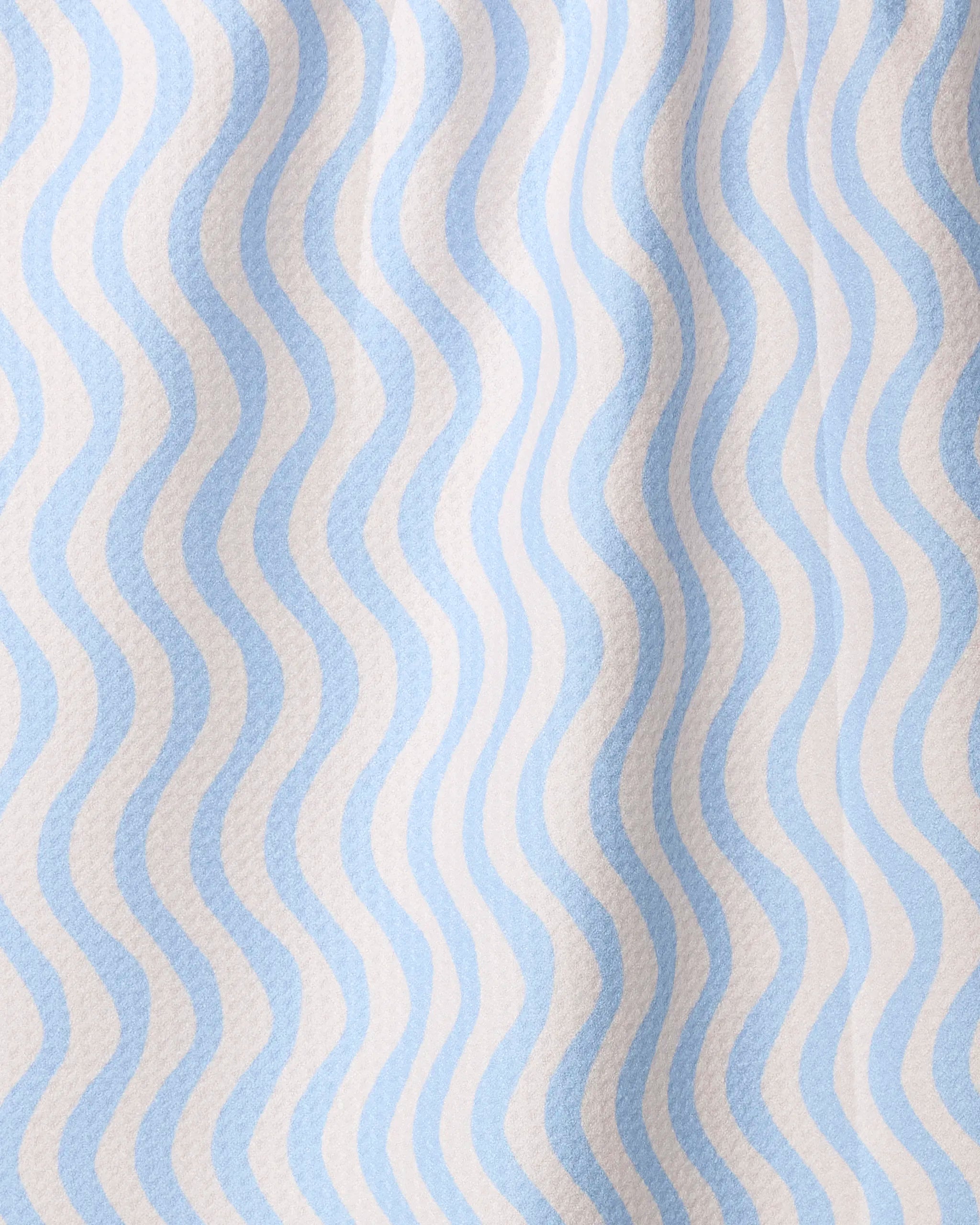 A close-up of Geometry’s Spatial tea towel shows its quick-drying, recycled fabric with wavy blue and white stripes and a textured, slightly wrinkled surface.