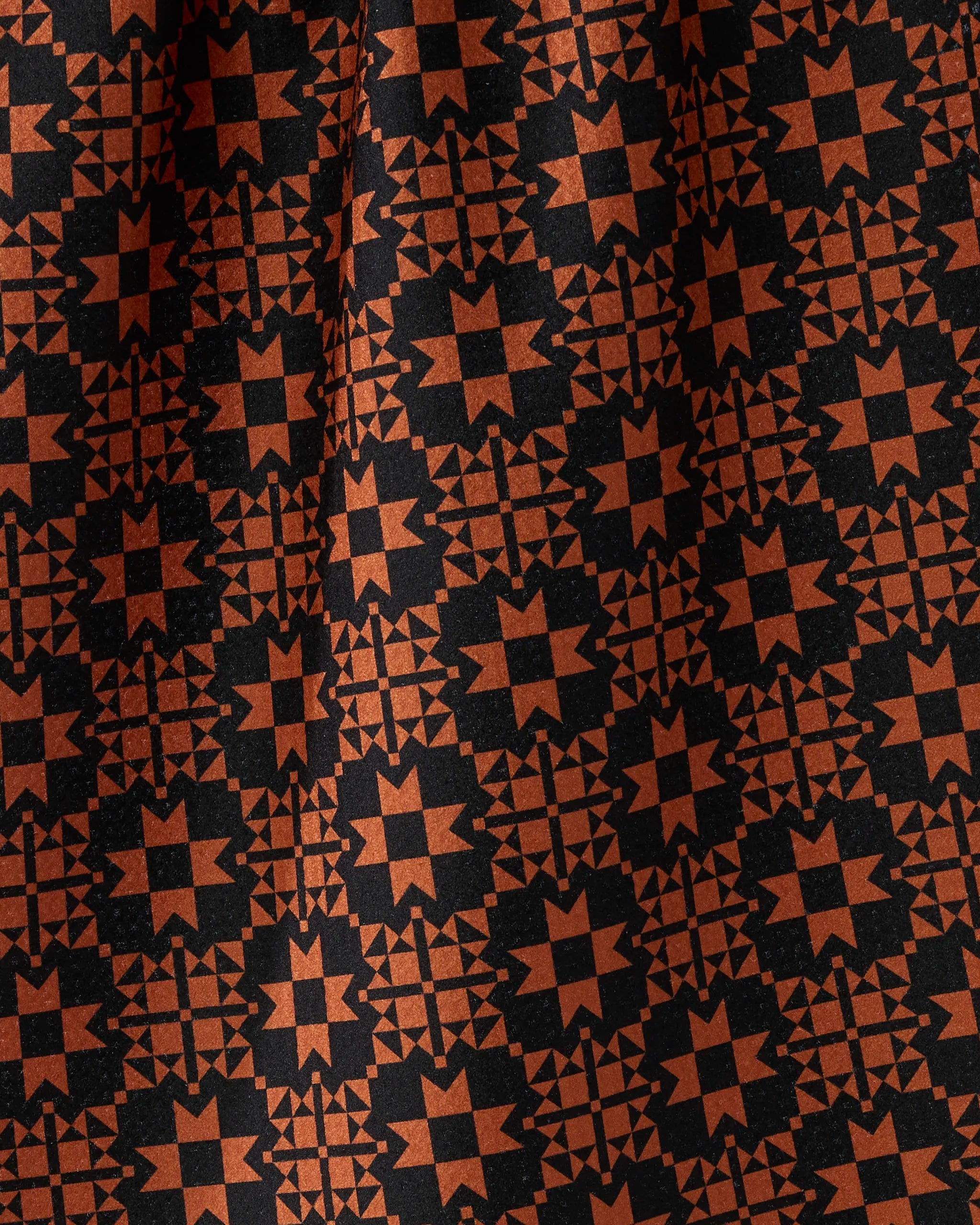 Spellwork by Geometry features bold orange geometric star patterns on black fabric. Crafted from recycled materials, this absorbent kitchen towel combines symmetry and texture for a striking, eco-friendly addition to your kitchen.