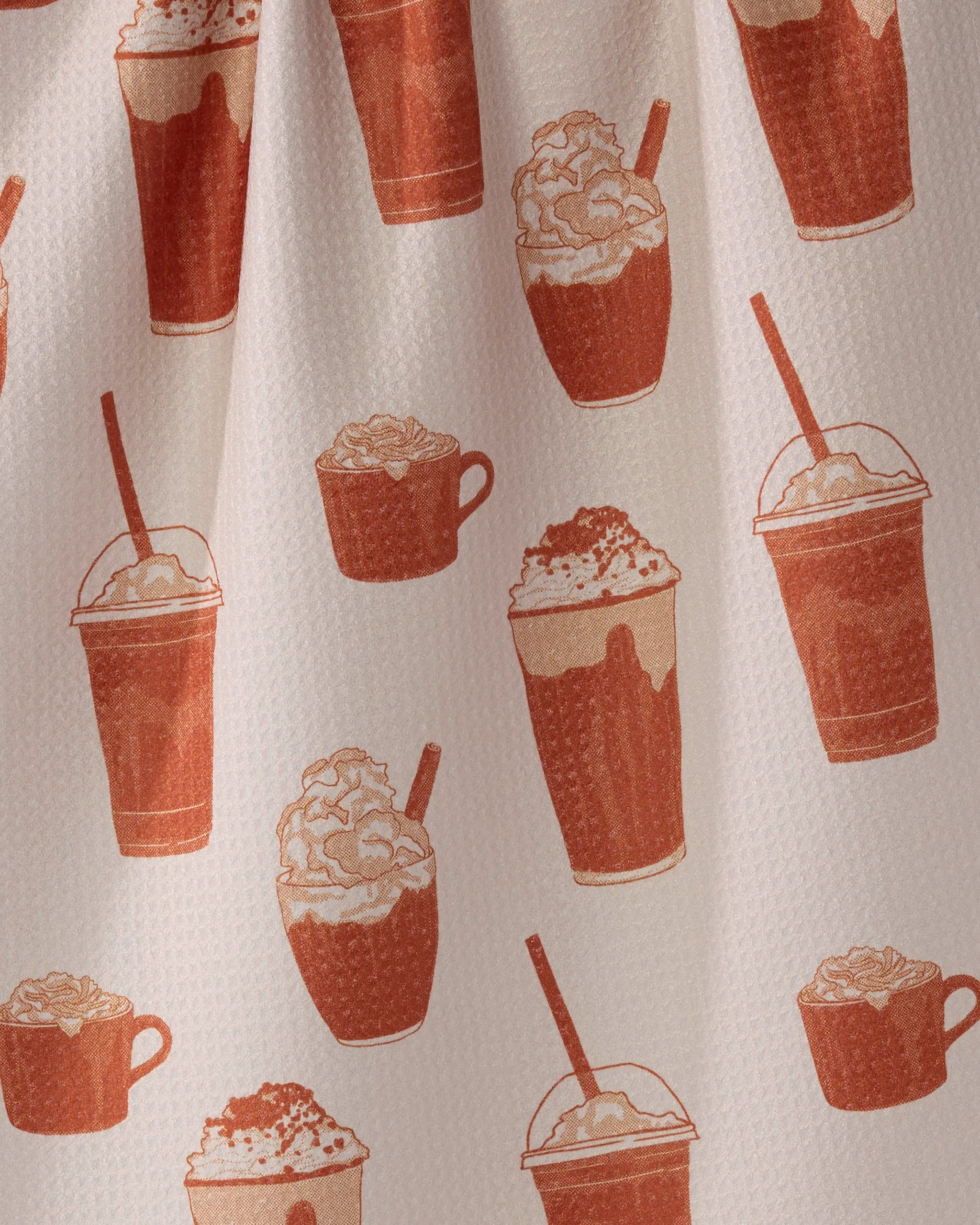 The Spice Season tea towel by Geometry features a pattern of coffee drinks, with cups and takeaway cups topped with whipped cream and straws, in brown and cream hues.
