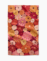 The Spicy Pumpkins tea towel by Rebecca Bobko features a vibrant pattern of overlapping circular flowers in red, pink, orange, and yellow on white, and is made from quick-drying recycled materials.