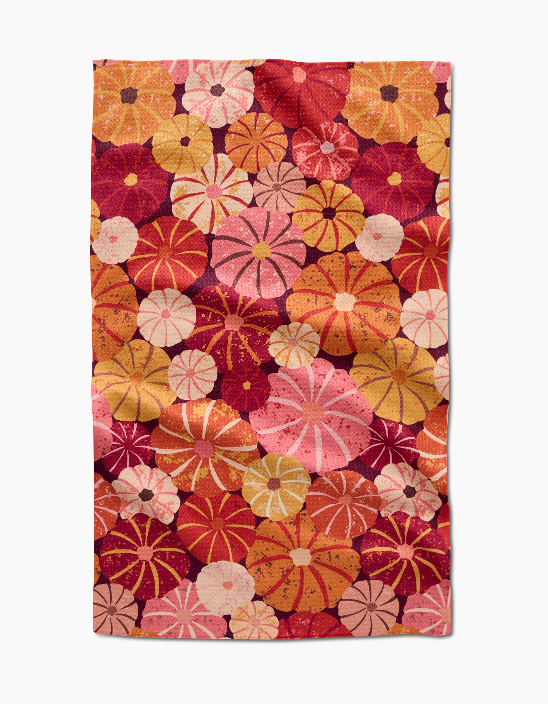 The Spicy Pumpkins tea towel by Rebecca Bobko features a vibrant pattern of overlapping circular flowers in red, pink, orange, and yellow on white, and is made from quick-drying recycled materials.
