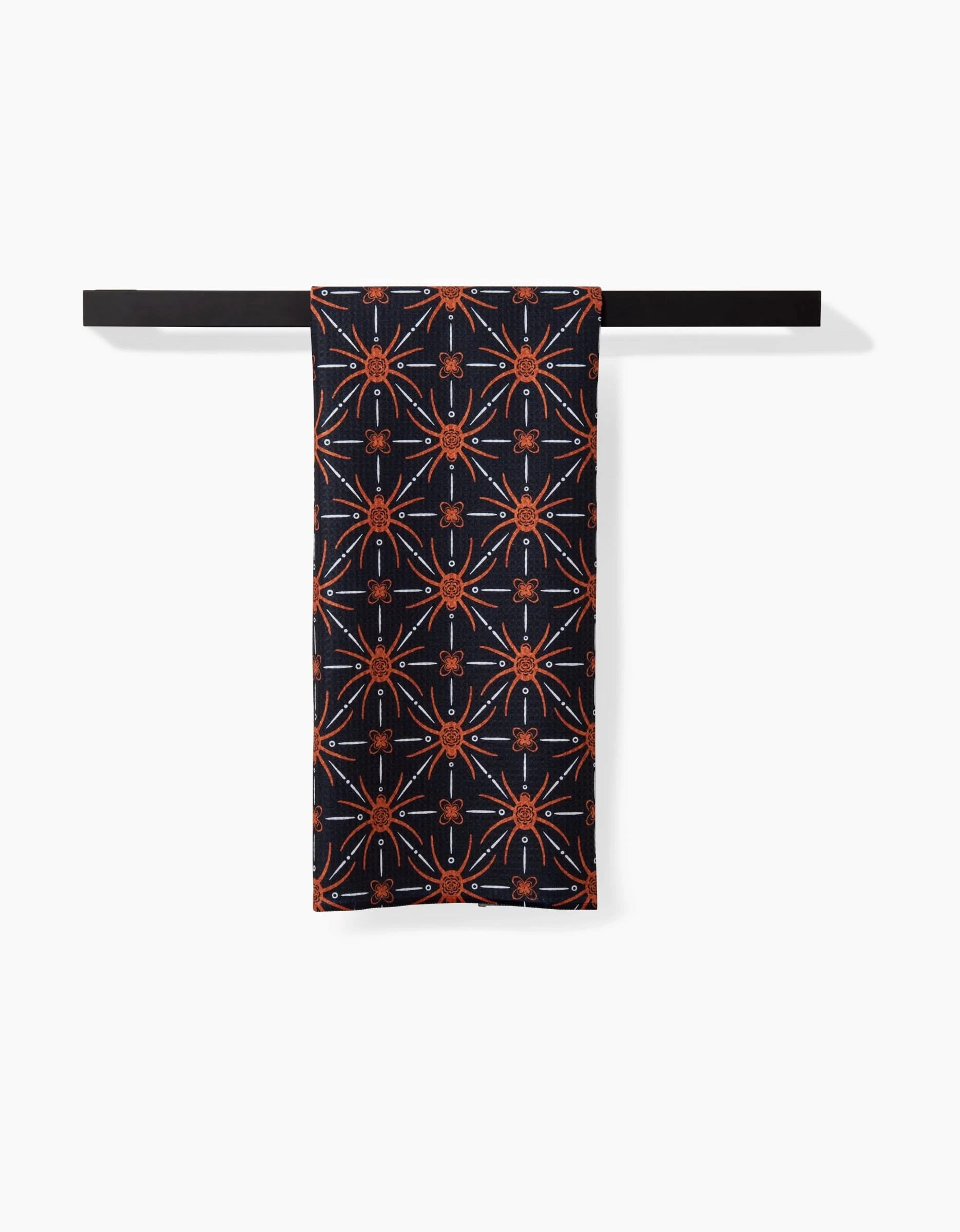 The Spider Geometric towel by Sarah Daugherty, featuring an orange and red geometric design, hangs neatly over a black rod against a plain white background.