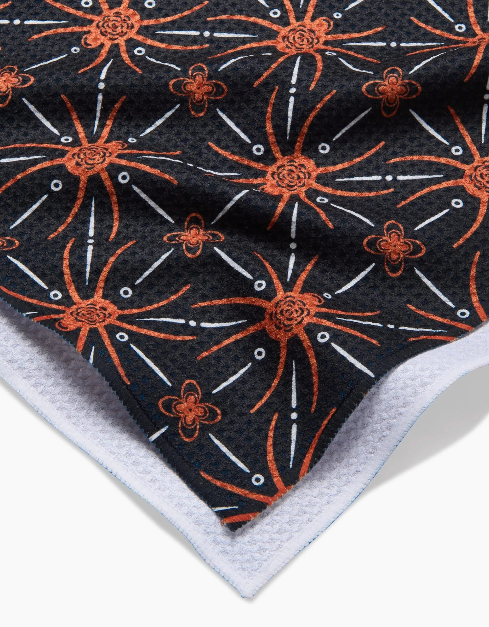 A close-up of the Spider Geometric by Sarah Daugherty shows its dark Geoweave™ fabric featuring an orange and white geometric floral pattern, a textured white edge, and detailed surface design.