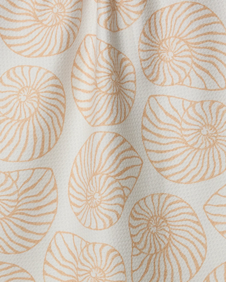 The Geometry Spira tea towel features beige, seashell-inspired spiral patterns on a textured white fabric with gentle folds, creating soft shadows and an organic, natural look.