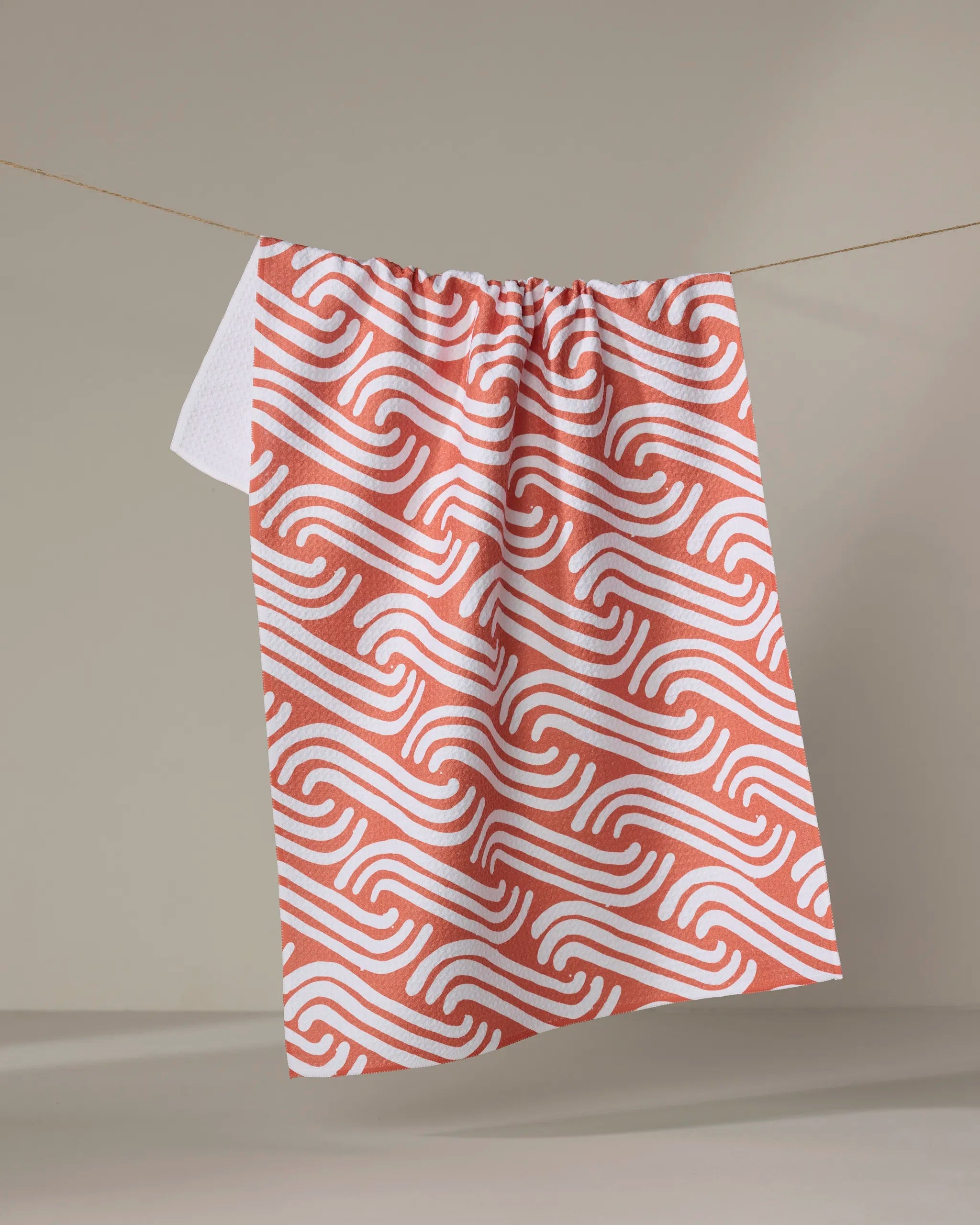 The Sissy Moon "Spirited" dish towel, featuring an absorbent red and white wavy geometric pattern, hangs on a clothesline against a neutral background.