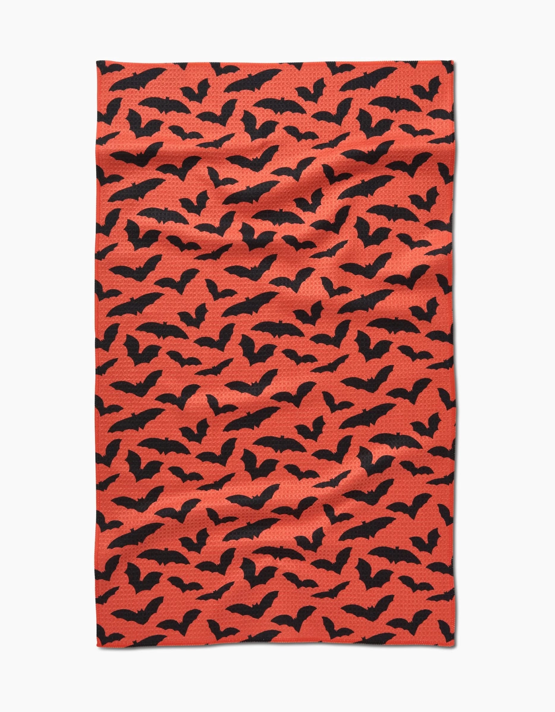 The Spooky Bats tea towel by Rebecca Bobko is rectangular, made from recycled materials, and features a black bat pattern on an orange background for a festive Halloween touch. The fabric shows a slightly wrinkled texture.
