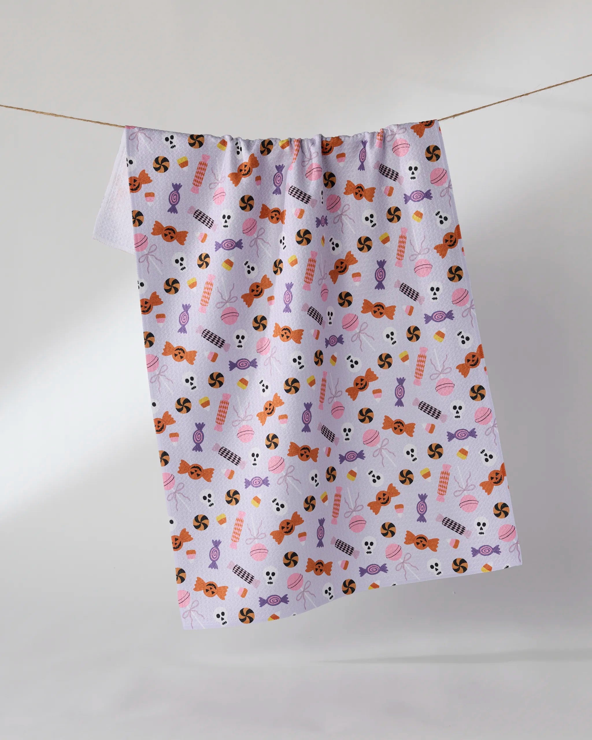 The Geometry "Spooky Sweets" tea towel, featuring a colorful candy pattern on white, hangs on a clothesline against a plain light background.