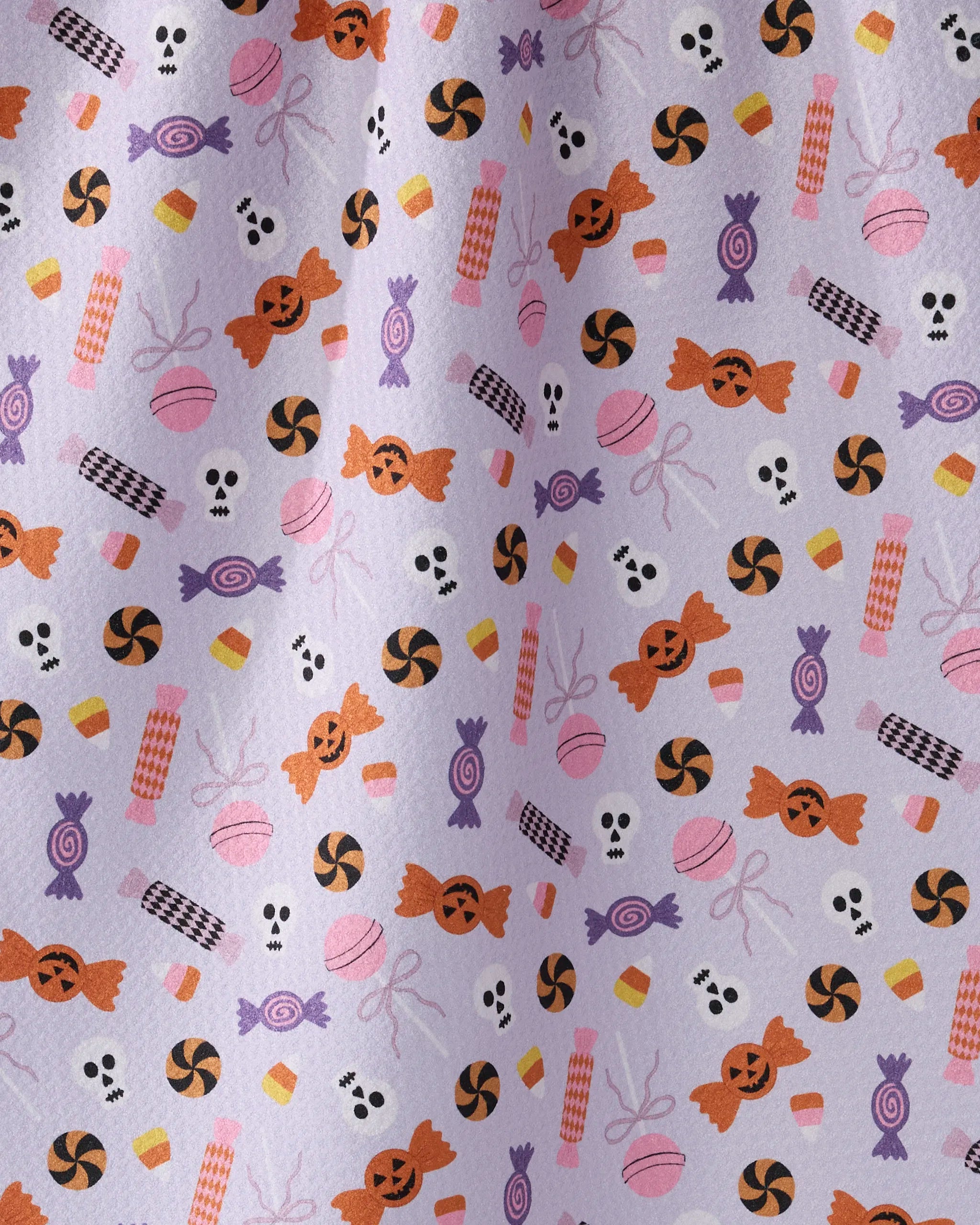 The Geometry Spooky Sweets kitchen tea towel features Halloween-themed candy such as orange pumpkins, skulls, candy corn, purple sweets, and striped candies on a light purple background.