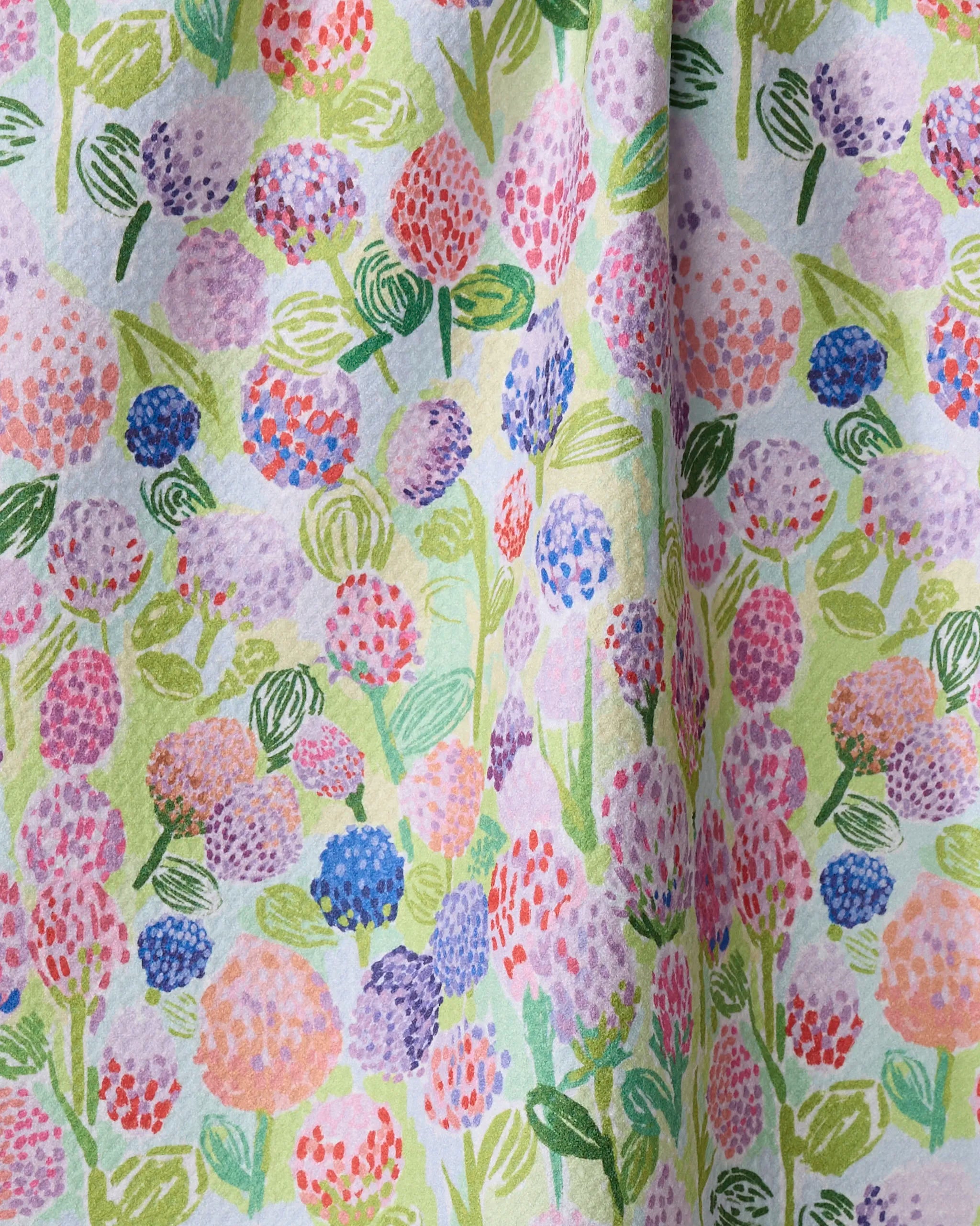 The "Spring Clovers" kitchen towel by Elisabeth Wing features a colorful painted floral pattern with pink, purple, red, and blue flowers on light green. Made from recycled materials for an eco-friendly touch.