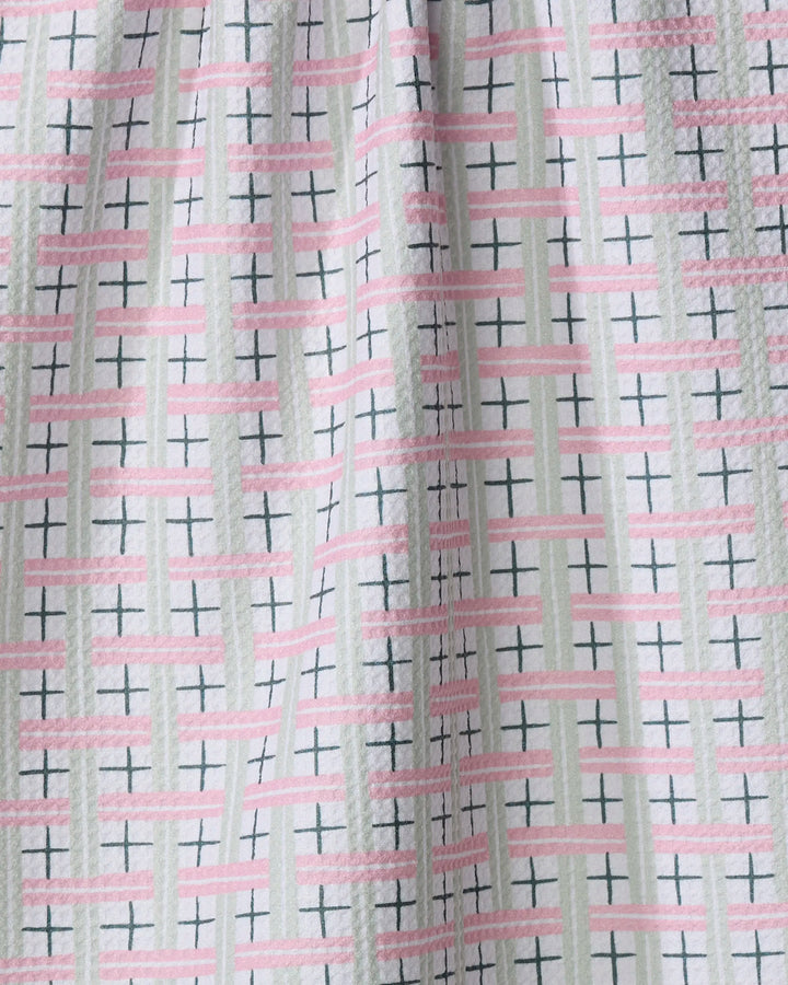 A close-up of the Spring Cottage Plaid tea towel by Hufton Studio, featuring recycled materials and a white textured background with geometric pink stripes, light green lines, and black crosses.