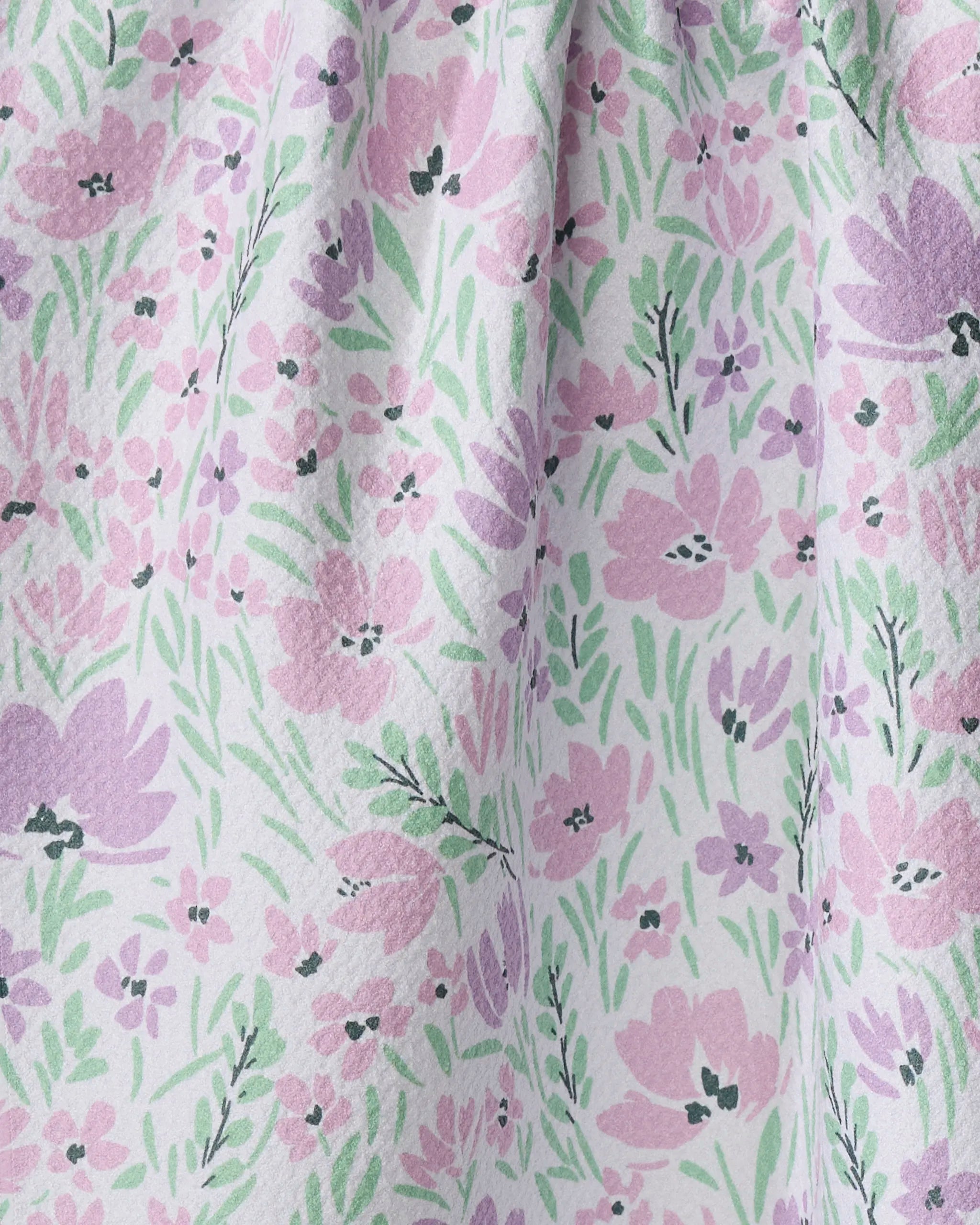 A close-up of Hufton Studio’s Spring Fleur Blooms tea towel shows a white background with pink and purple flowers, green leaves, and a slightly textured fabric made from recycled materials, gathered near the top.