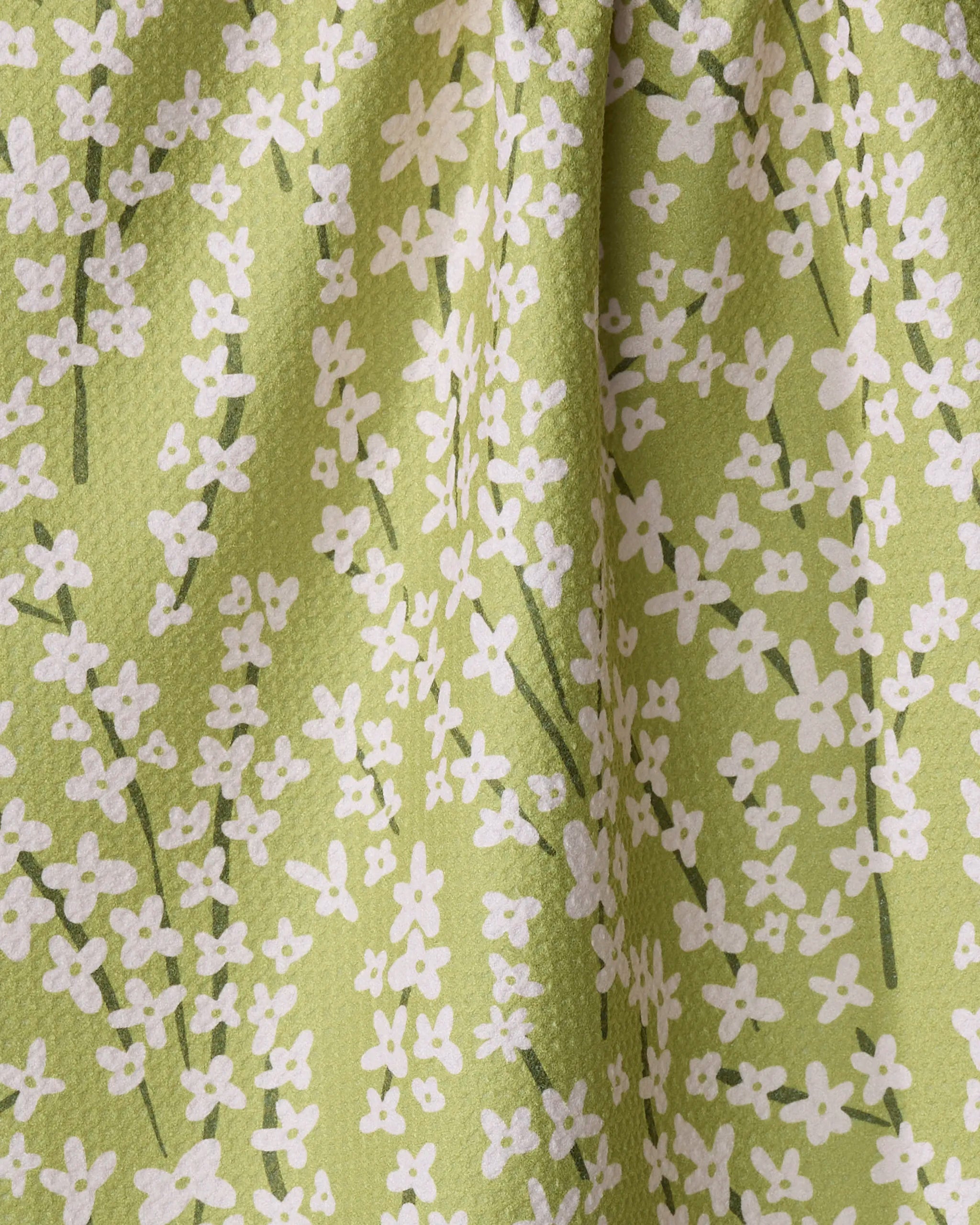 Kayla Ann's Spring Green Forsythia features green fabric with small white flowers and thin green stems, slightly wrinkled and textured—ideal as a recycled kitchen or tea towel.