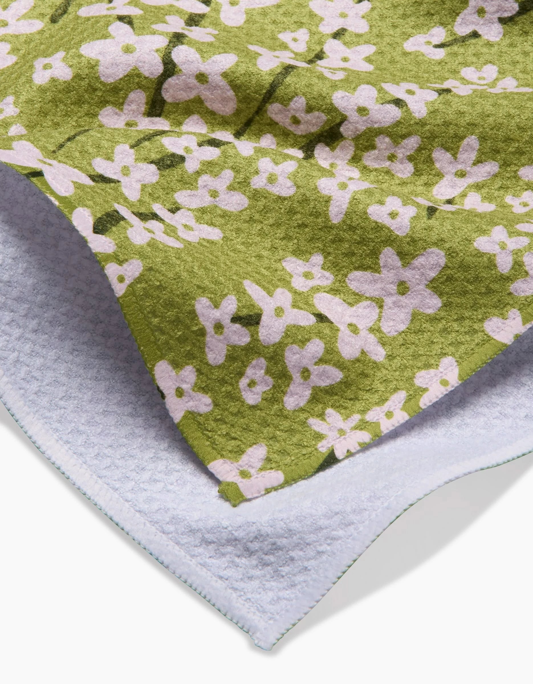 A close-up of the Kayla Ann Spring Green Forsythia ultra-absorbent towel, showcasing its green side with a pink floral pattern and a plain white textured Geoweave reverse, both edges visible.