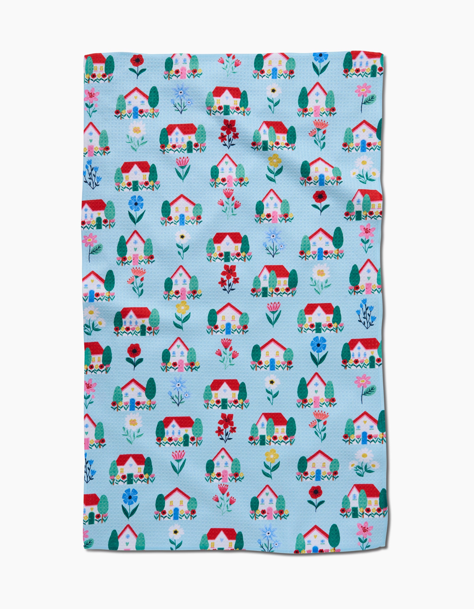 The Spring Houses blanket by Ceyda Alasar is light blue with a colorful pattern of houses, trees, and flowers in red, pink, blue, and green. Made from recycled materials for an eco-friendly touch.