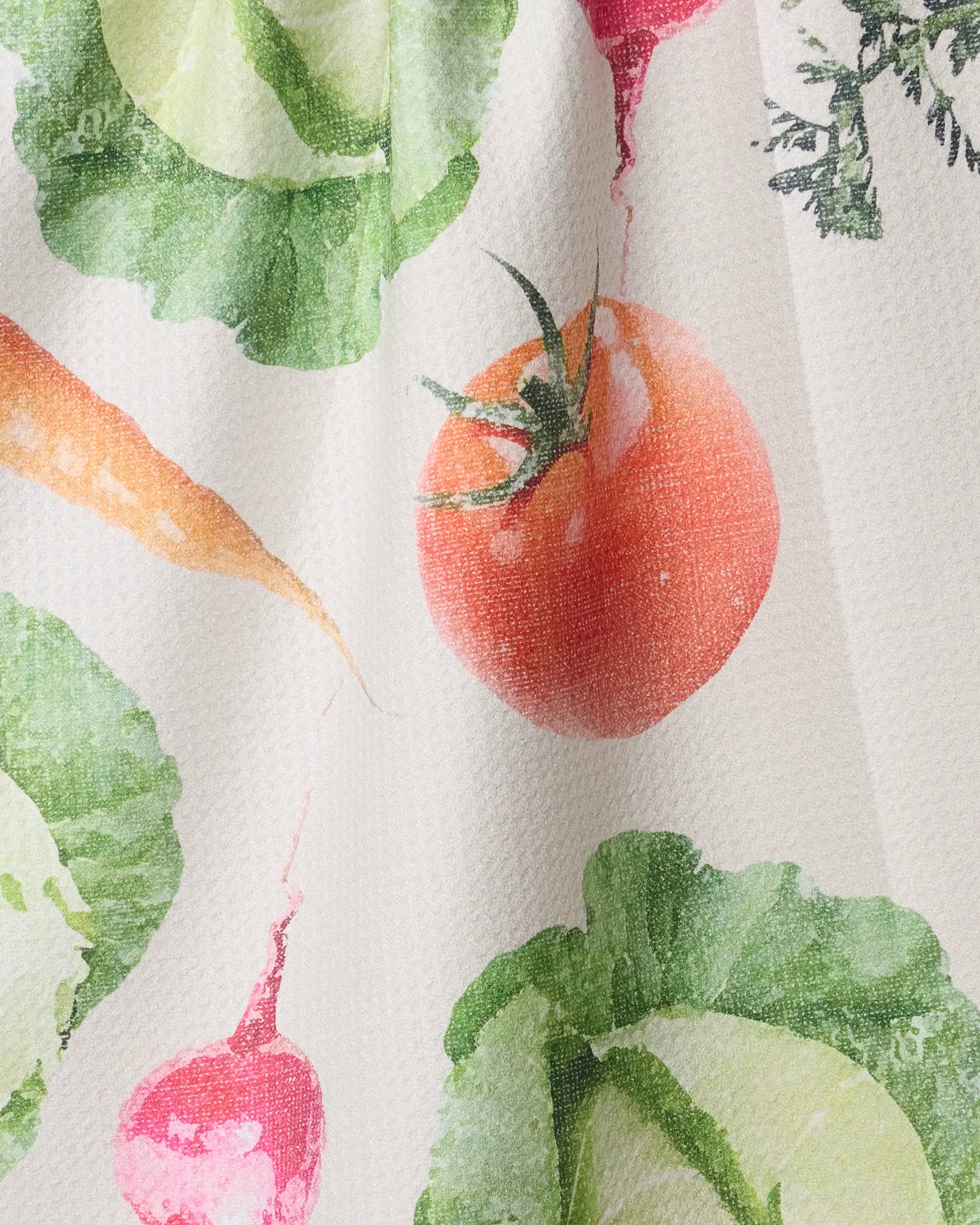 The "Spring Produce" tea towel by Geometry features a watercolor-style illustration of tomato, carrot, radish, and leafy greens printed on textured white fabric.