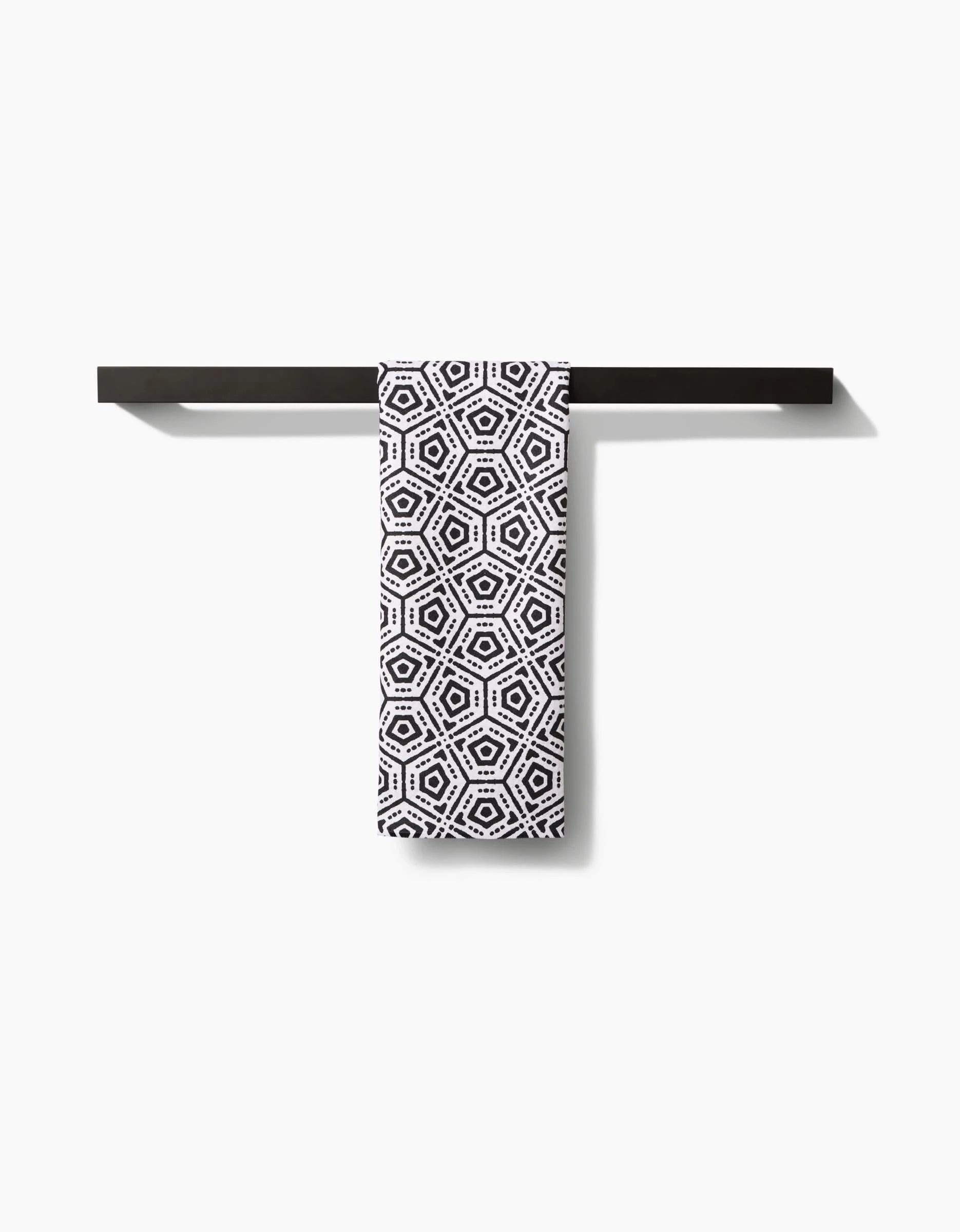 A black towel bar holds the Katherine Berkeley Squeezebox tea towel, featuring a black geometric hexagon pattern on white Geoweave™ fabric, set against a plain white background.