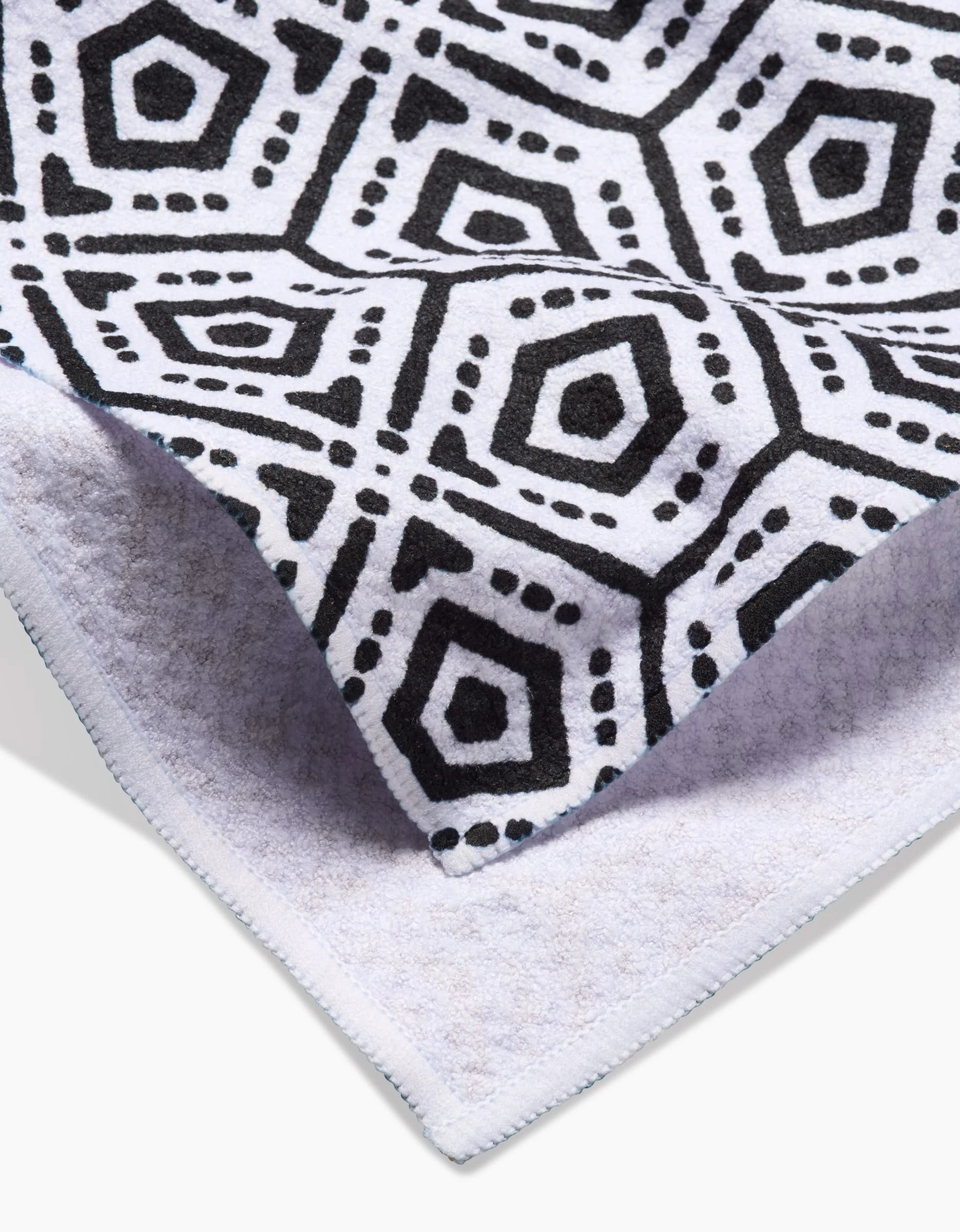 A close-up of Katherine Berkeley’s Squeezebox Tea Towel in Geoweave™ fabric, showing a black hexagon and dotted pattern on white, with its textured front and plain light back both visible.