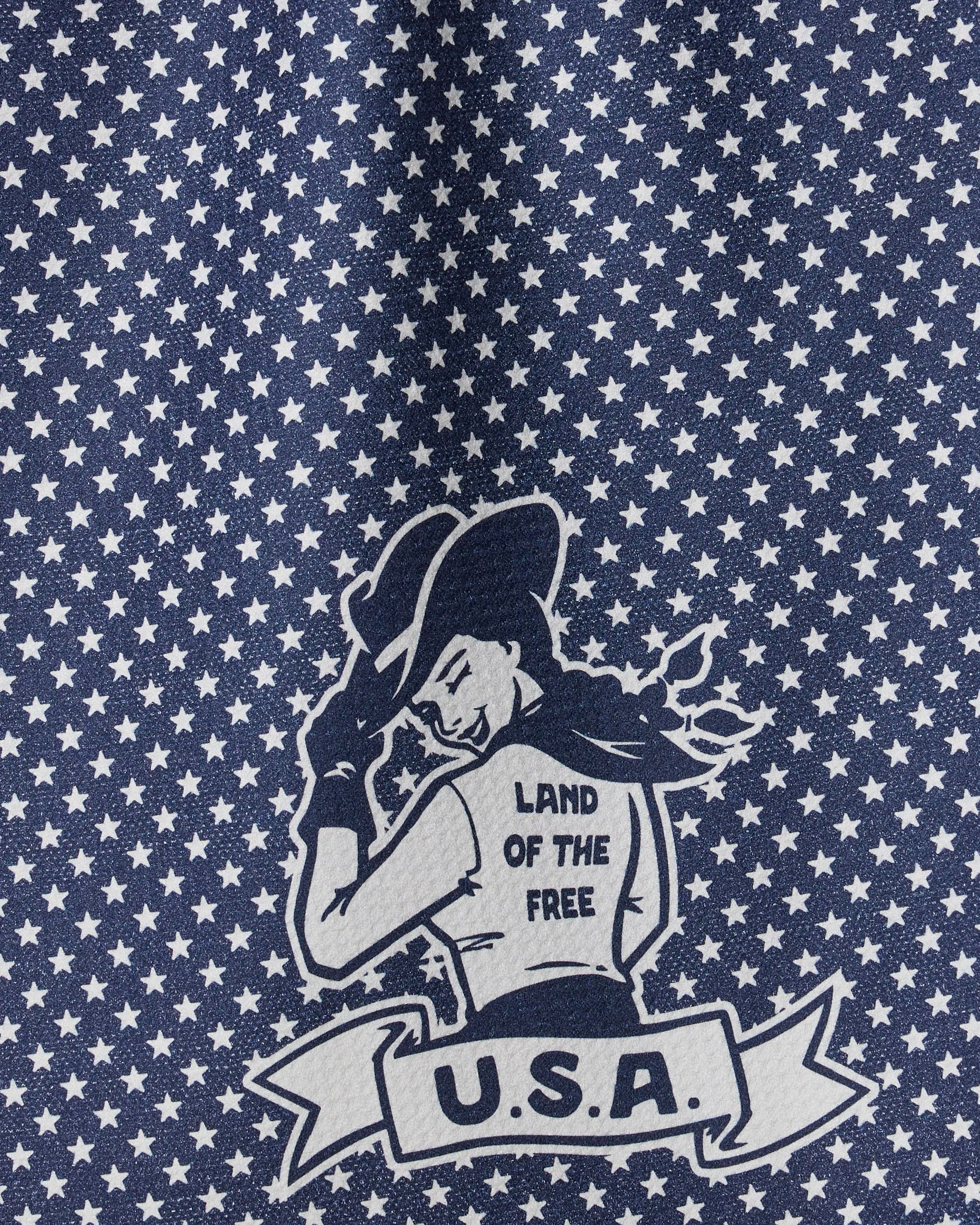 The Geometry "Star Cowgirl" tea towel features a retro cowgirl tipping her hat, white stars on blue, and a banner reading "LAND OF THE FREE" and "U.S.A." Made from ultra-absorbent recycled materials.