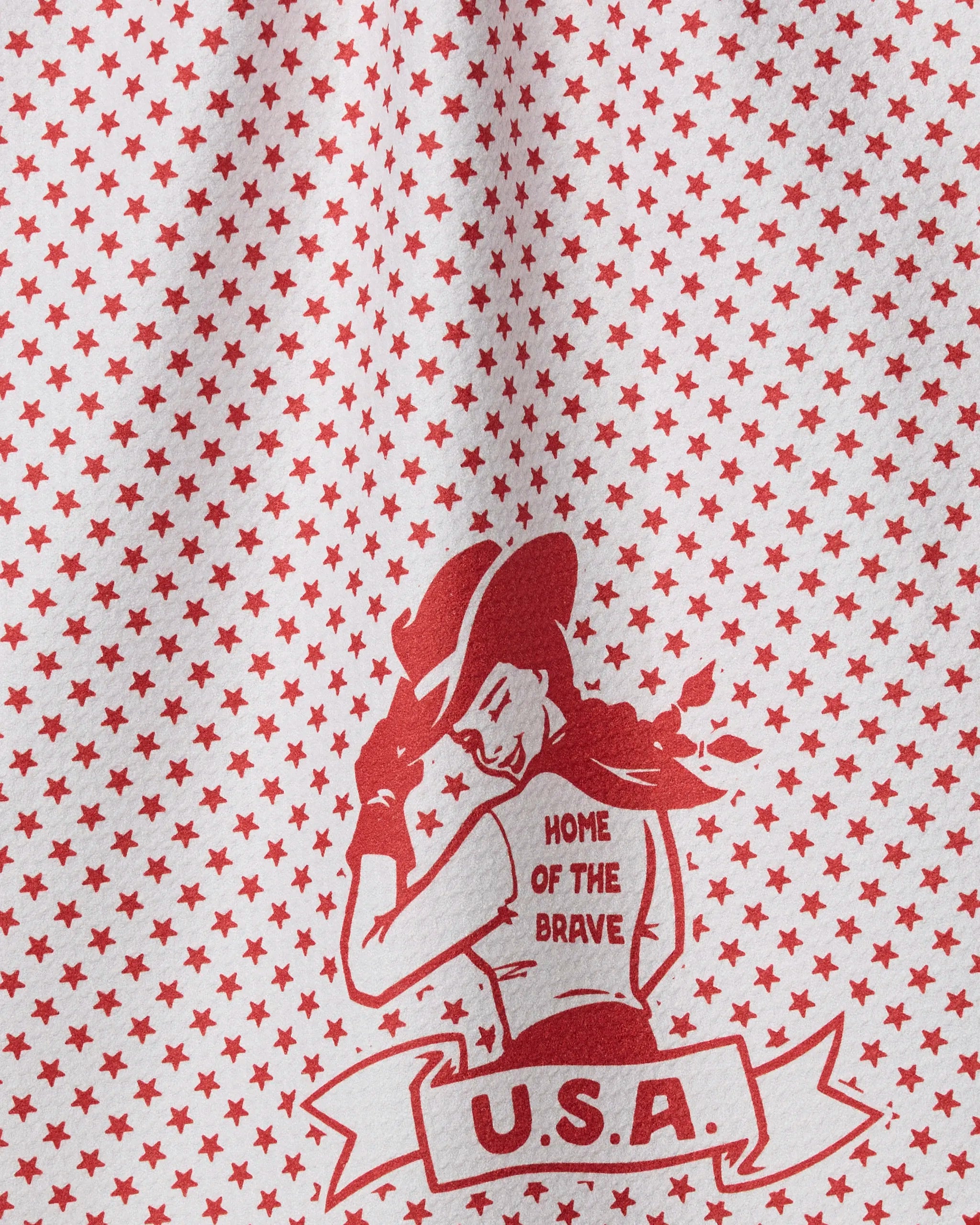 The Geometry Star Cowgirl tea towel features a red and white star pattern, a woman in a cowboy hat with "HOME OF THE BRAVE" on her back and "U.S.A." below, all made from recycled materials.