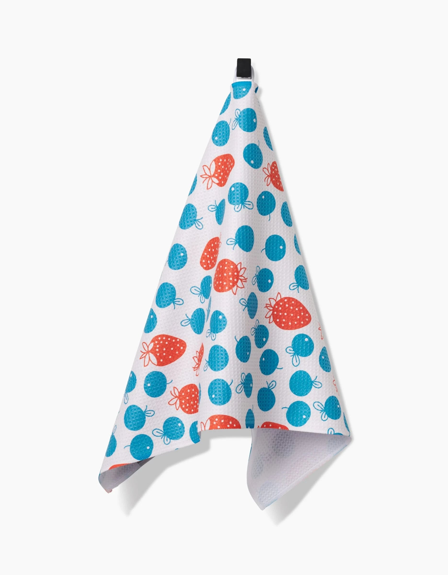 The Sara Mari Star Spangled Berry tea towel hangs from a black loop, with red strawberries and blue blueberries on Geoweave fabric, set against a light background.