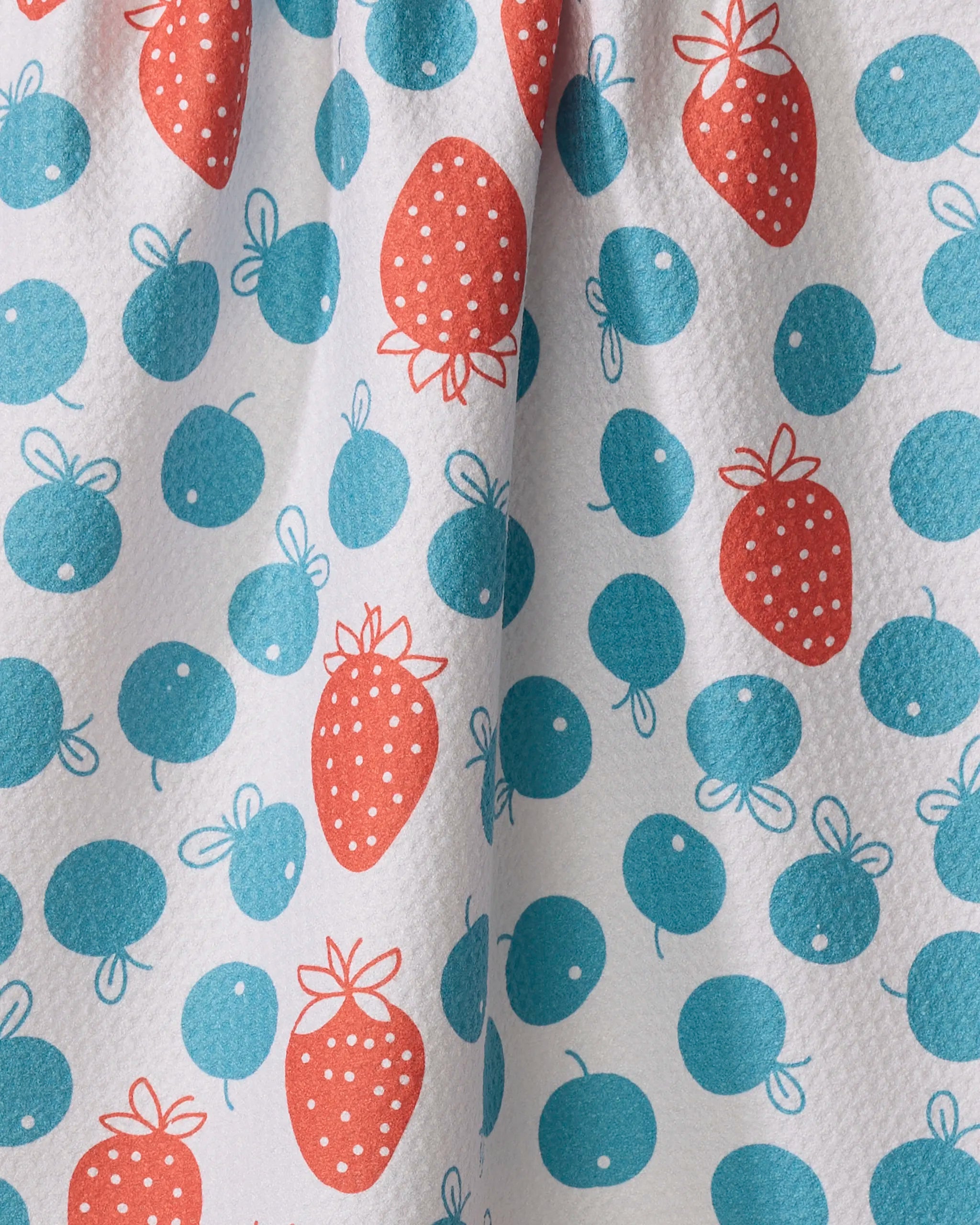 The Sara Mari "Star Spangled Berry" tea towel features a white fabric with blue circles and red strawberry motifs, outlined in simple lines. Its ultra-absorbent, dimpled surface displays gentle folds for added texture.