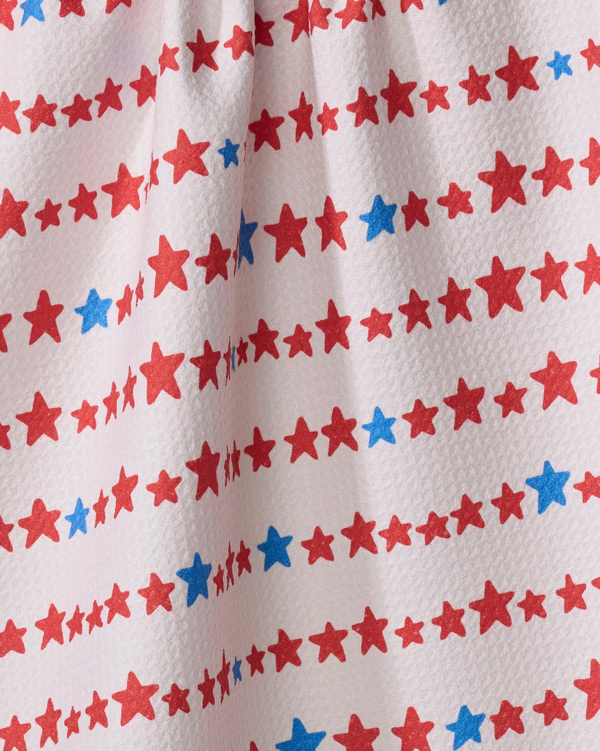 Kayla Ann’s Starry Stripes tea towel features red and blue stars in horizontal rows on white fabric with a crinkled texture. The bold red stars pop, making it a stylish and absorbent dish towel for your kitchen.