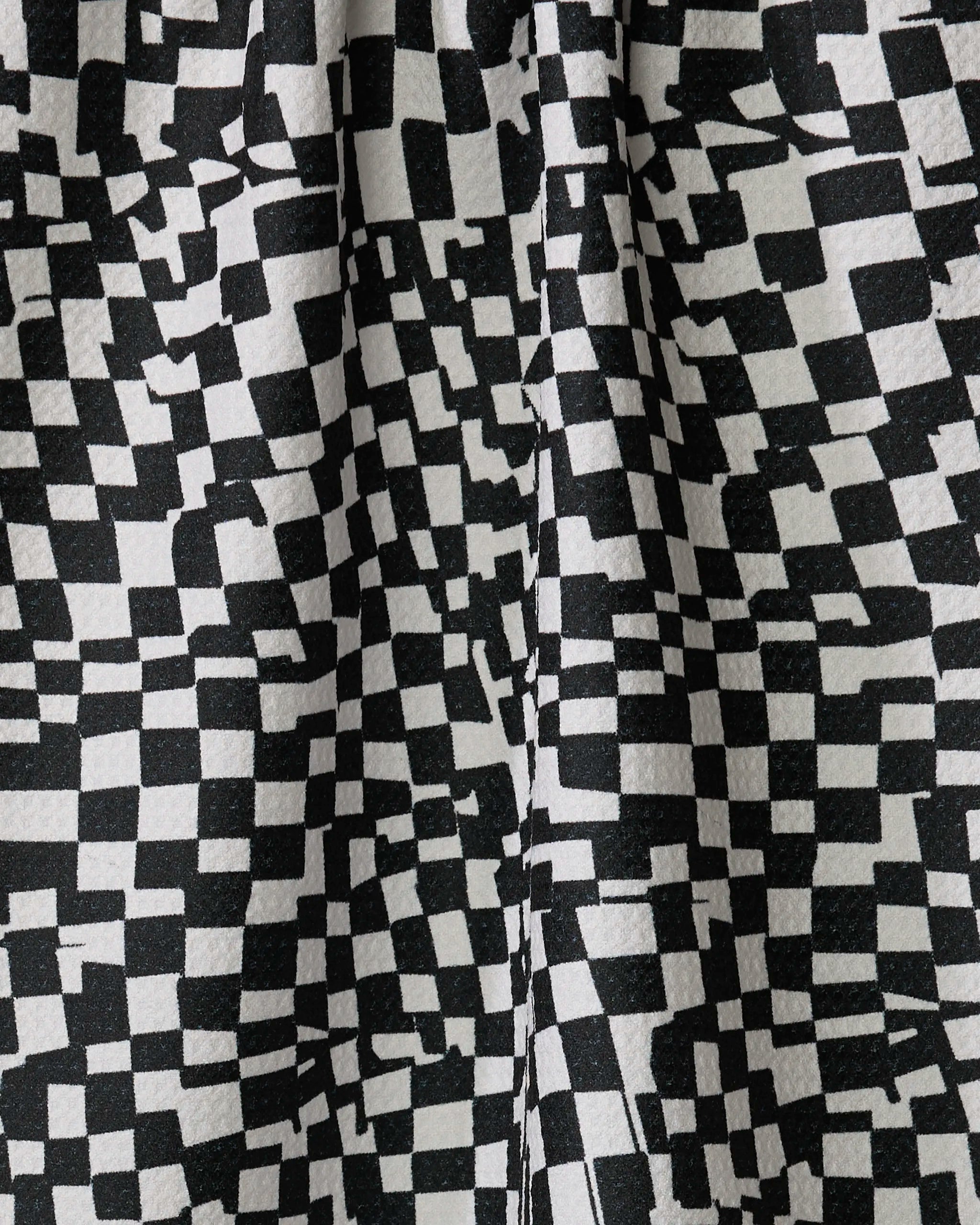 Close-up of the Geometry "Static" kitchen towel, showcasing its black and white irregular checkerboard pattern with uneven squares and textured folds—expertly crafted from recycled materials.