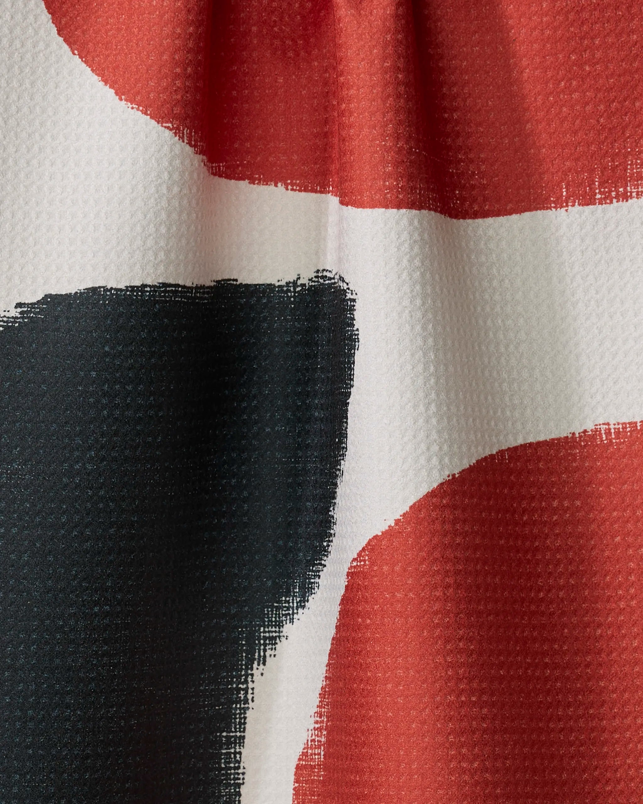 Close-up of Geometry’s Still tea towel shows textured, dimpled fabric with abstract red, black, and white shapes. Large painterly color blocks create a bold pattern. Made from recycled materials for eco-friendly appeal.