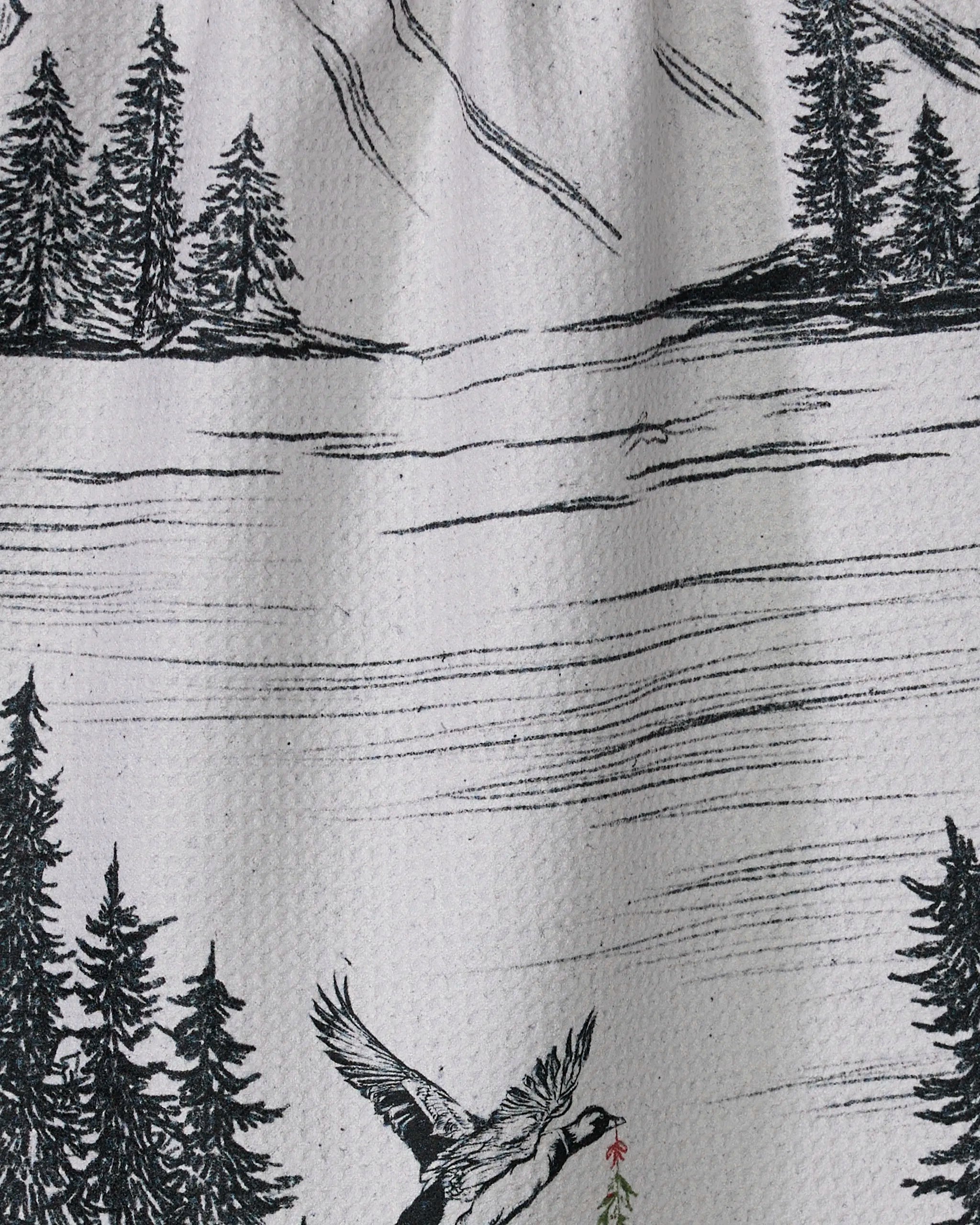The Stillpine tea towel by Geometry features a black and white mountain landscape with pine trees, a lake, and a bird carrying a branch—crafted from recycled materials and perfect for your kitchen.