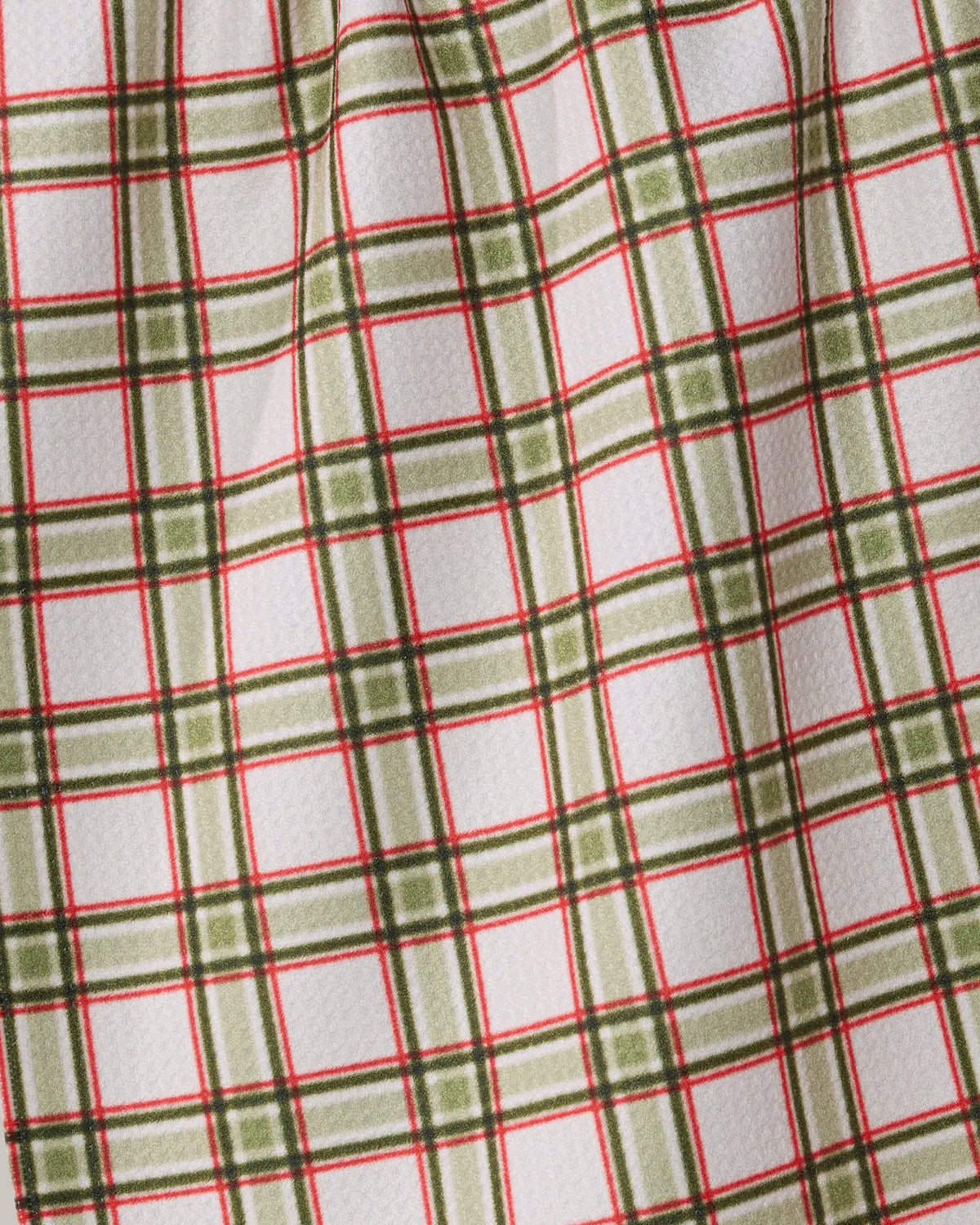 The Stocking Plaid by Geometry features a white base with a green and red plaid pattern. Crafted as an ultra-absorbent towel, its slightly wrinkled texture creates subtle folds and shadows across the checkered design.