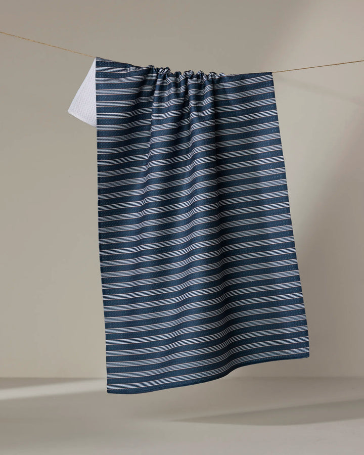 The Buy Guide's Straight Across - Navy dish towel, featuring blue and white horizontal stripes, hangs slightly gathered at the top over a clothesline against a neutral background.