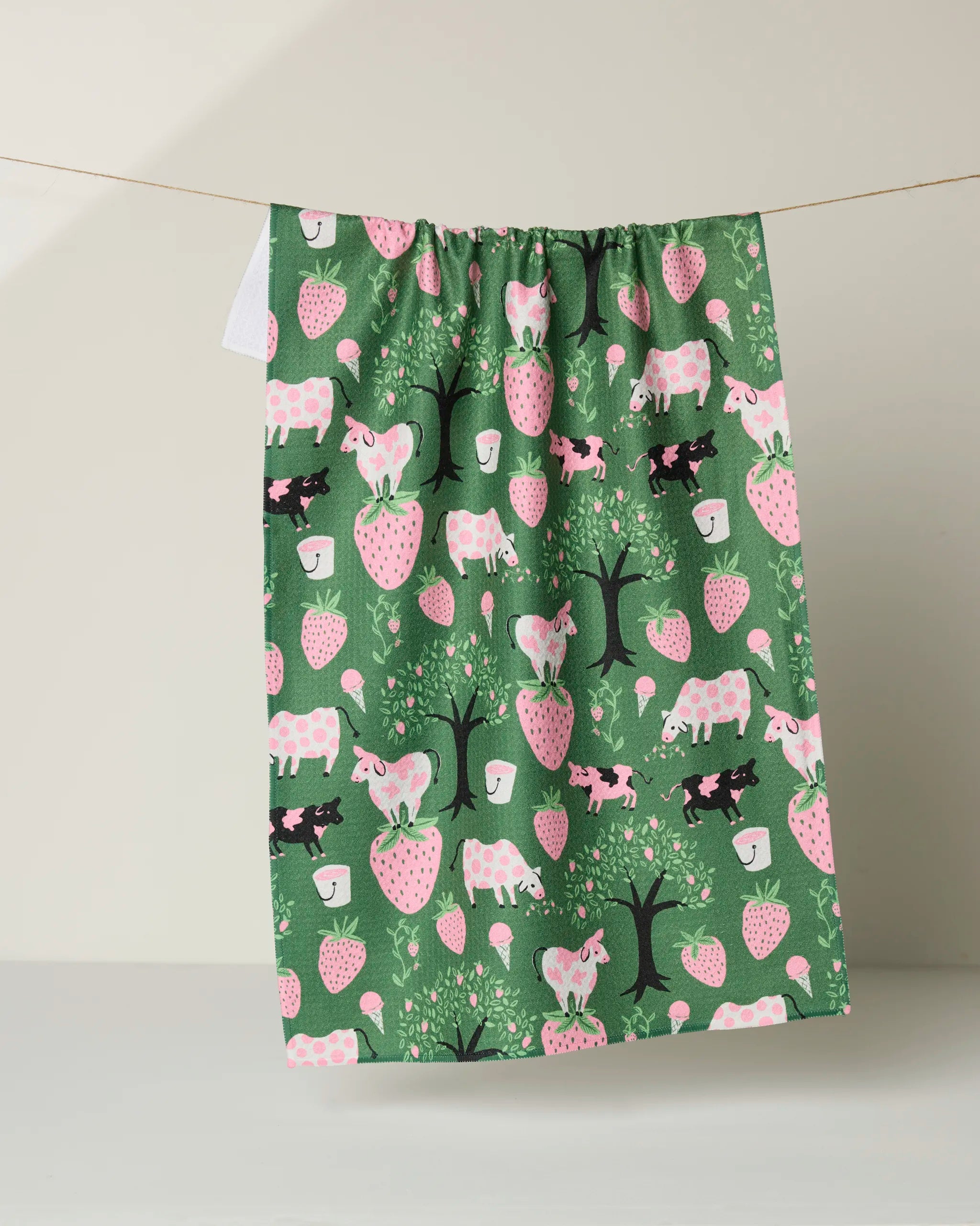 The Louise Pretzel "Strawberry Cows" dish towel is green, ultra-absorbent, and features pink and black cows, strawberries, coffee cups, and trees on a light background.