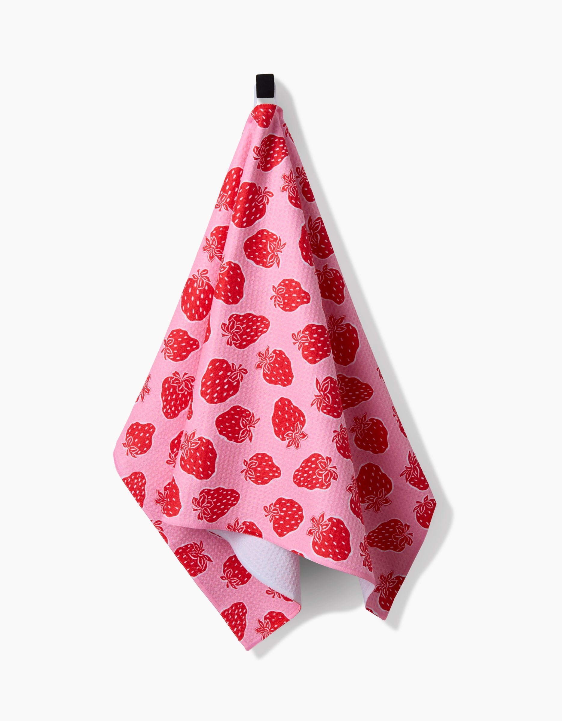 The Strawberry Fields tea towel by Charlie Rowan Designs features bright red strawberries on pink Geoweave fabric, hanging from a black loop against a white background.
