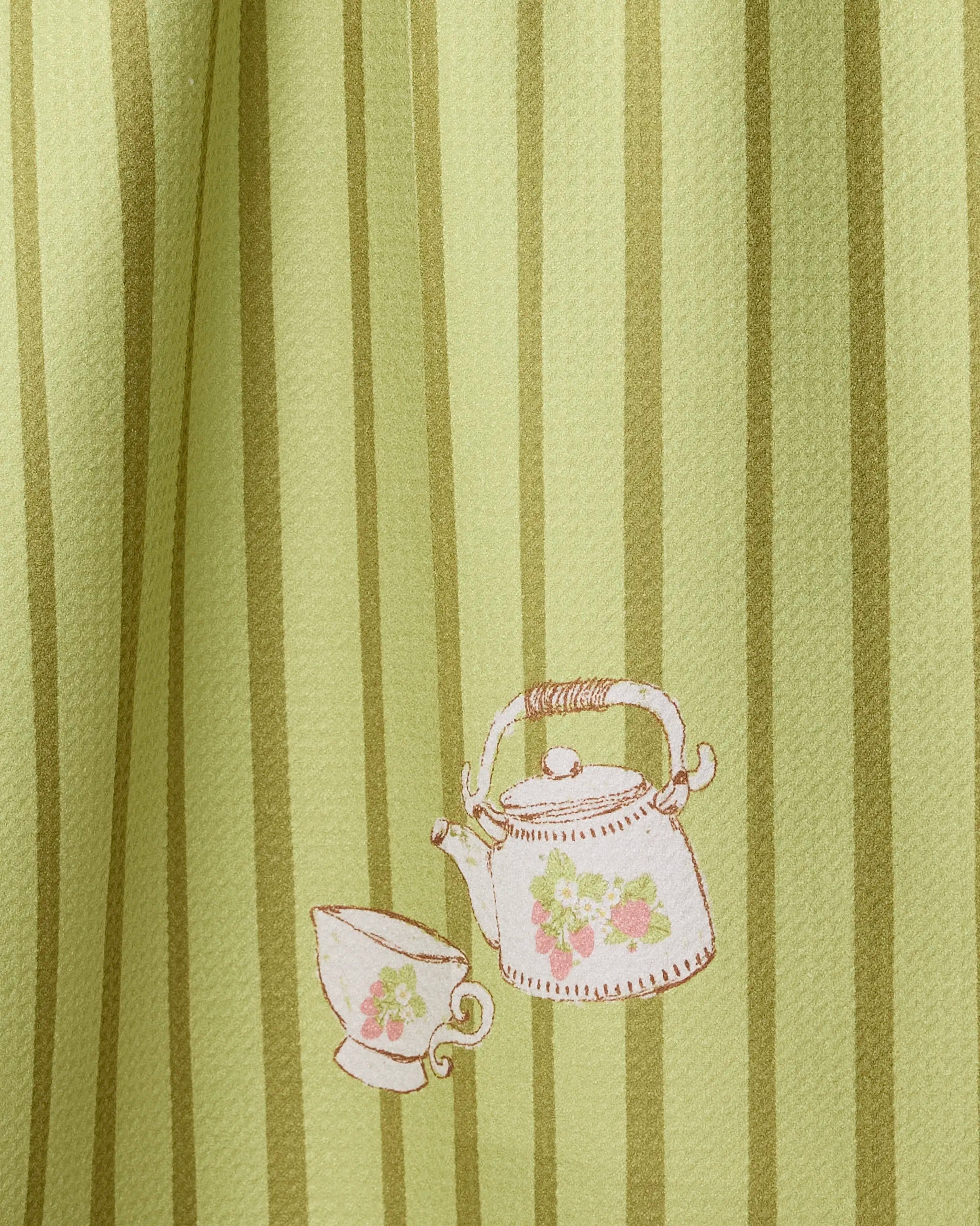 The "Strawberry Spring Green" kitchen towel by Geometry features green fabric with vertical olive stripes and a printed white teapot and teacup, both decorated with pink and green florals.