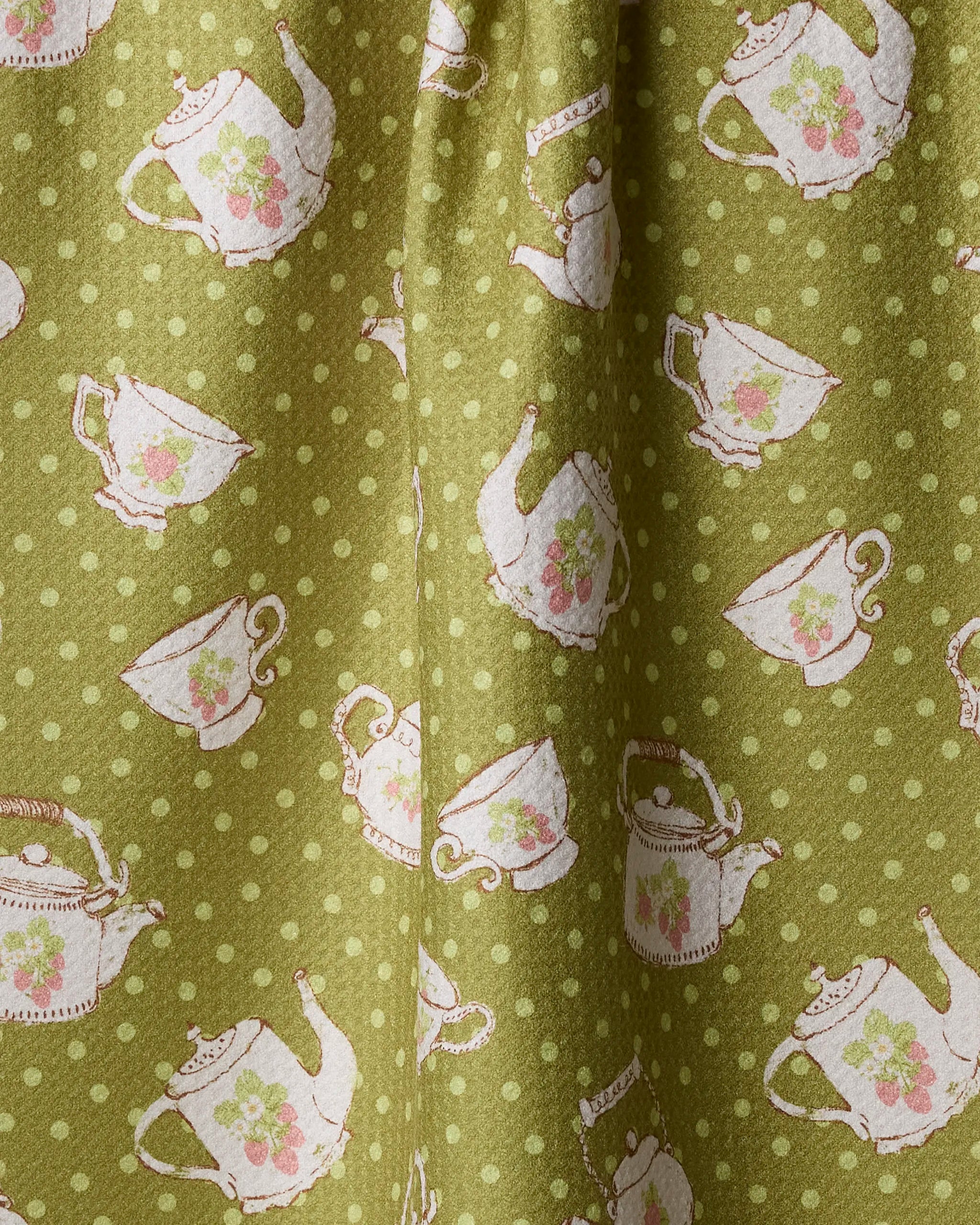 The Geometry "Strawberry Tea Green" recycled kitchen towel features green fabric with light green polka dots, white teapots and teacups accented by pink florals—an eco-friendly way to add charm to your space.